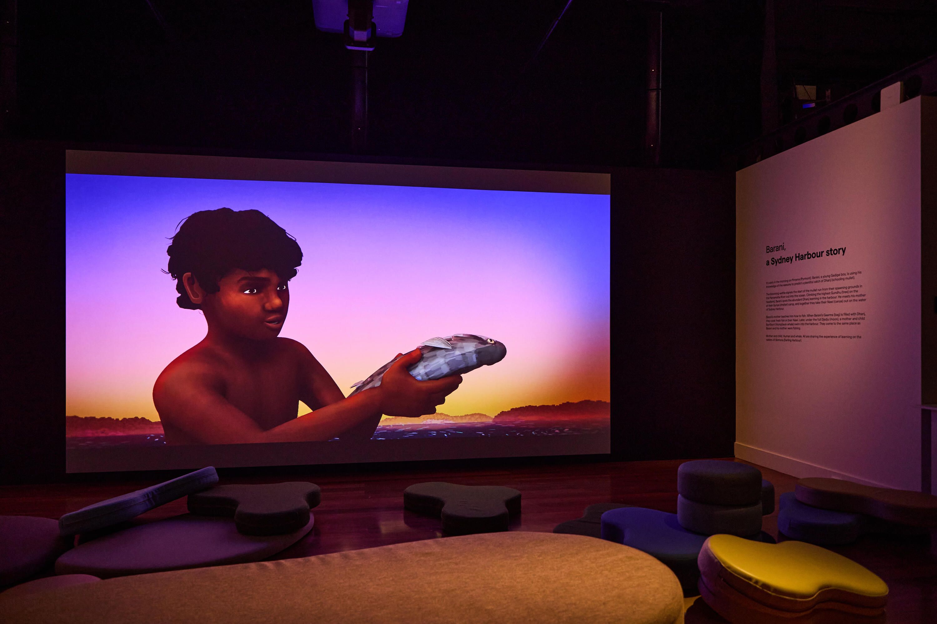 Photo of a museum exhibition space with curved soft seating and a large projection screen