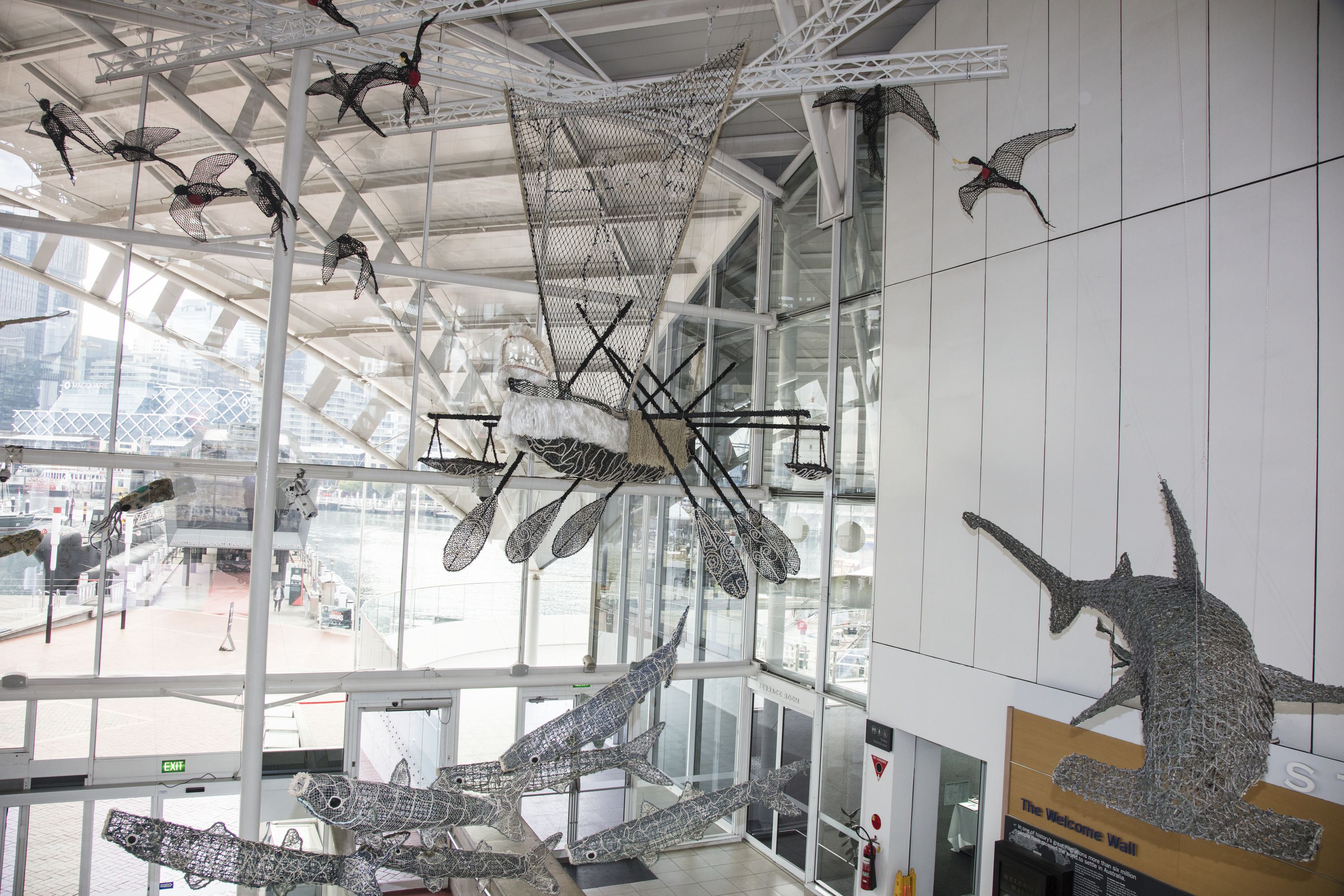 Sculptures of a large Ghost net canoe, surrounded by sculptures of flying birds, fish, and a hammerhead shark, is shown in final position above the museum's foyer.
