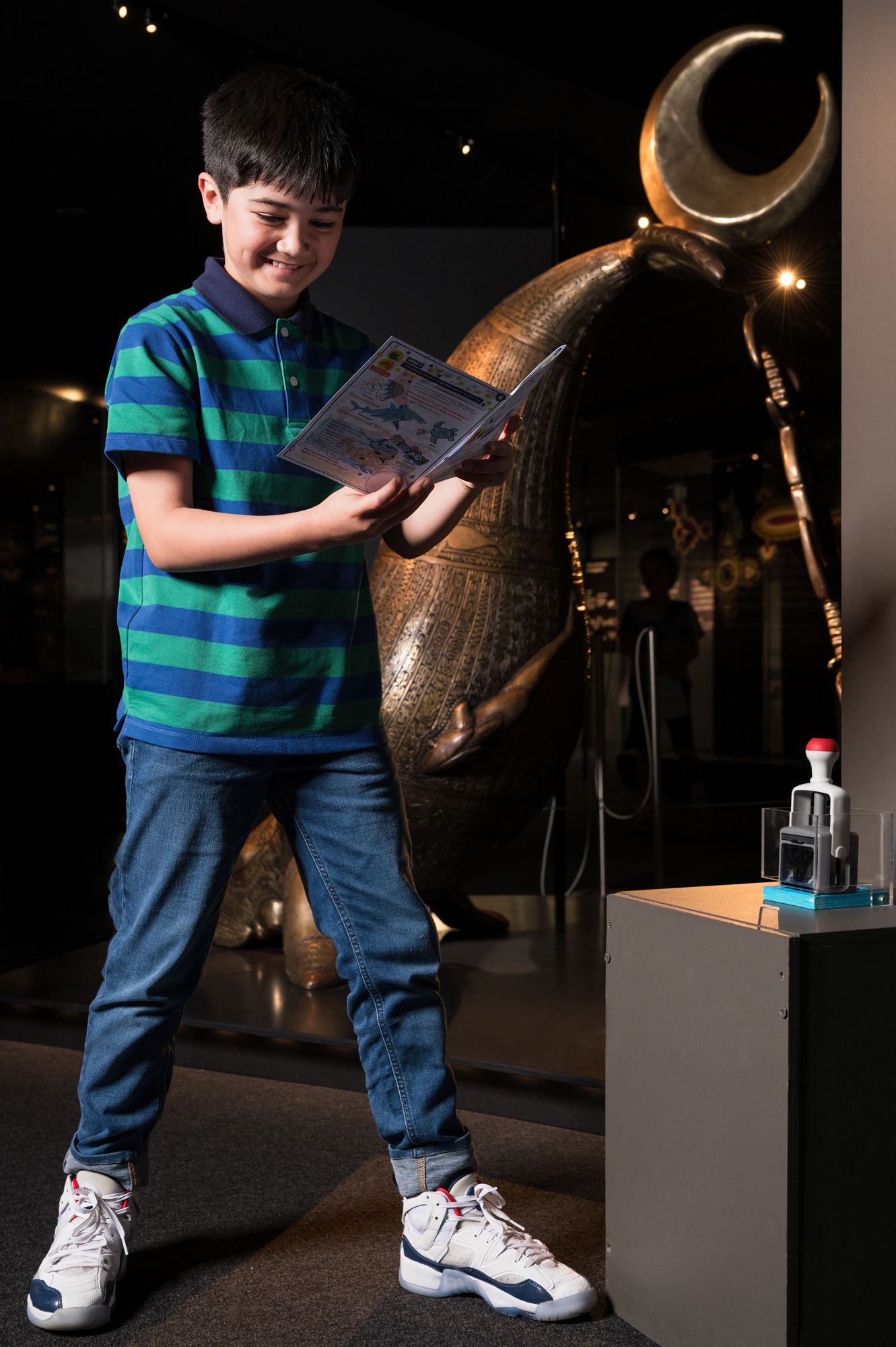 Photo of a boy standing in a gallery with a paper booklet.