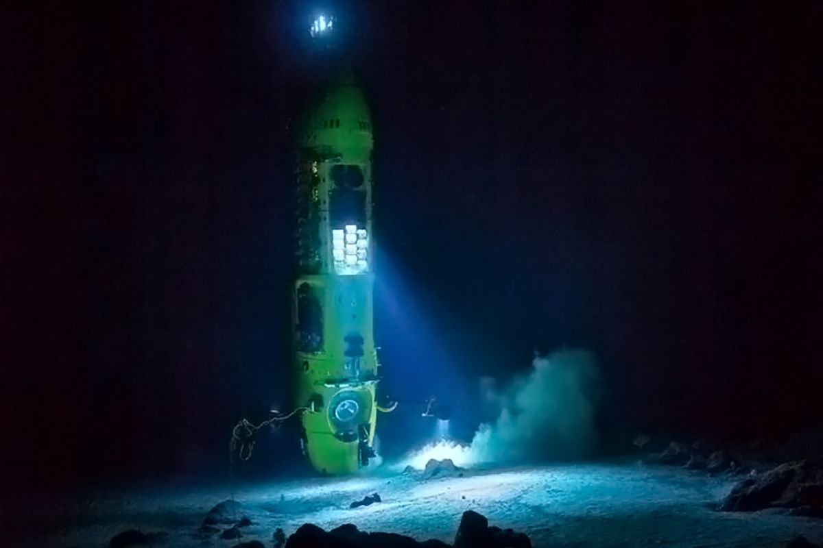Image in a dark space of a bright yellow/green sub with a bright light shining onto the ocean floor.