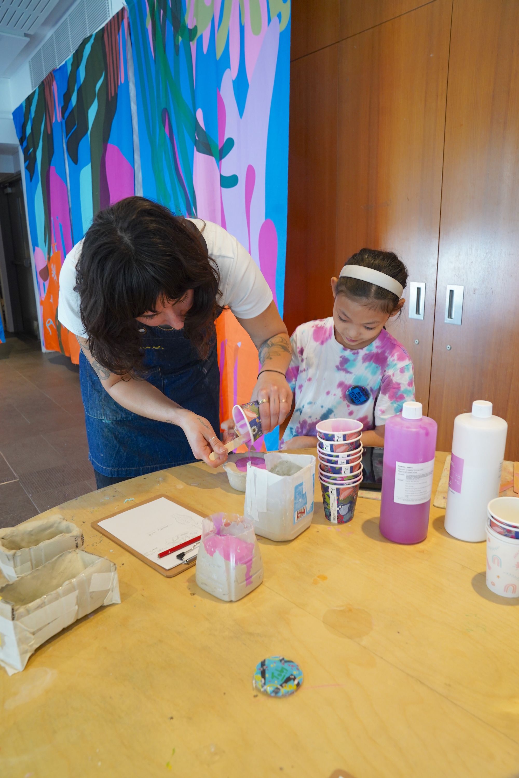 a lady and a girl standing behind a table working together on creating a mould for an artwok.