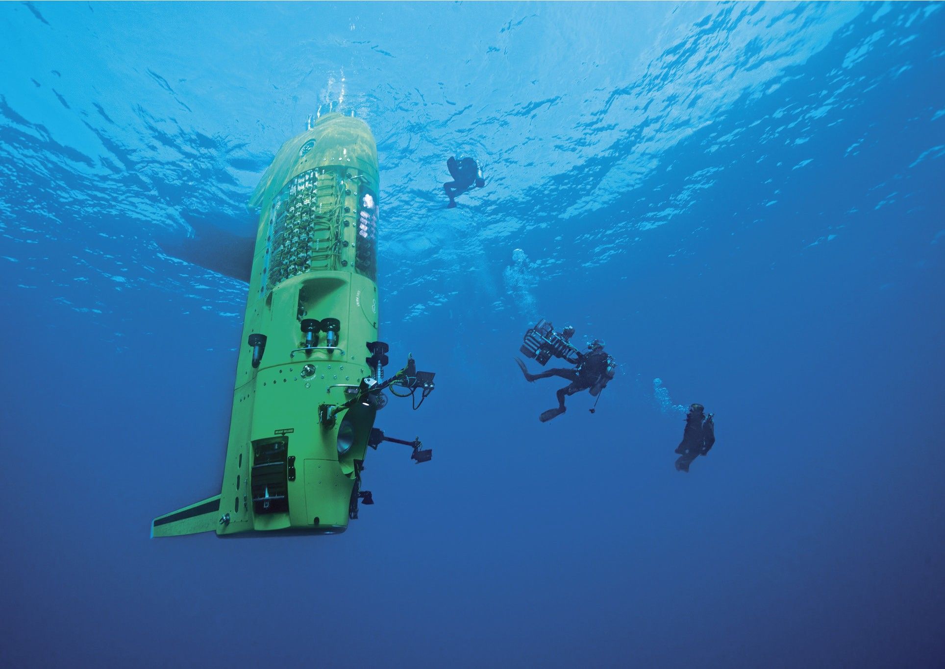 Photo taken underwater showing a yellow green submarine with Divers swimming around it