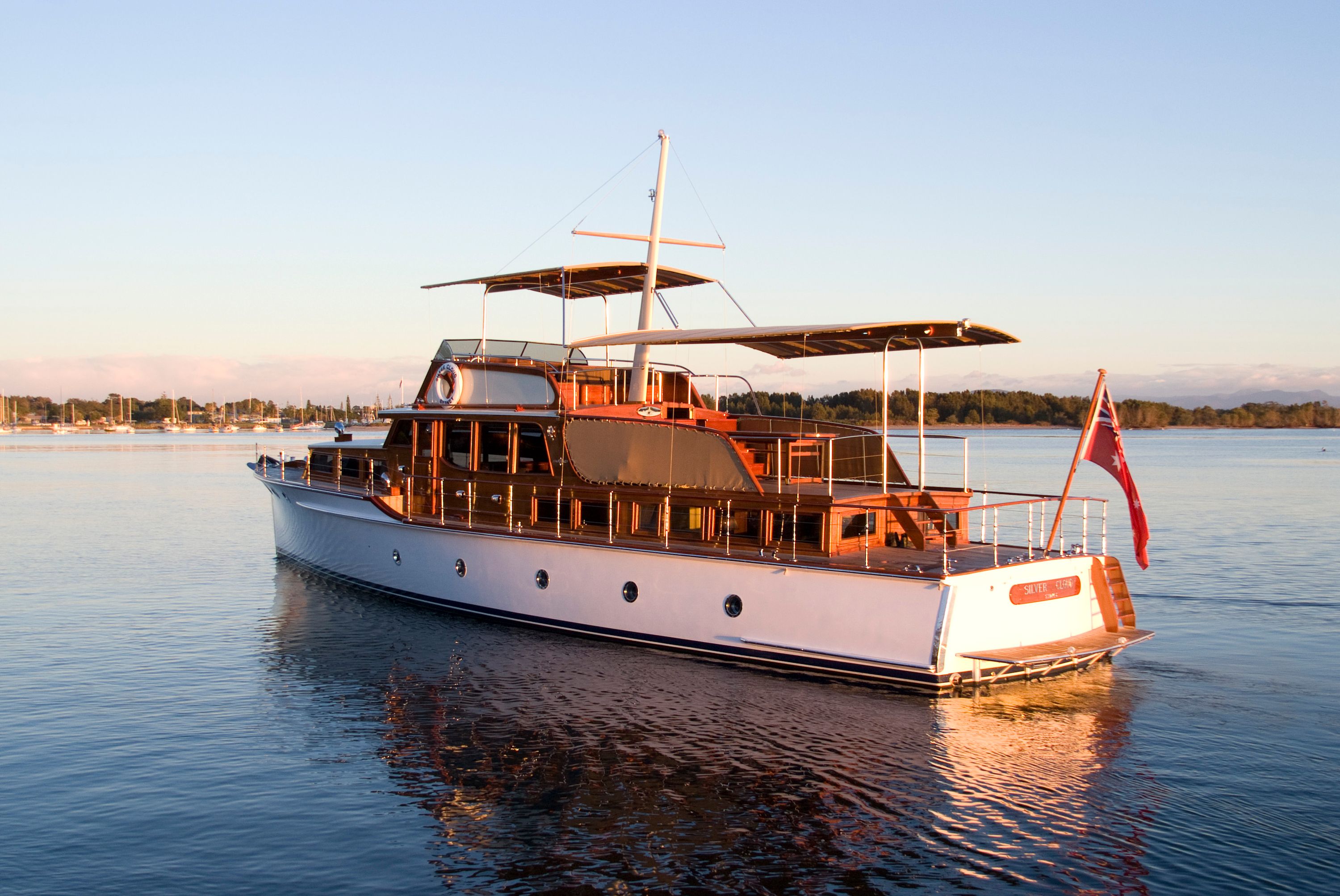 Photo showing the side a rear of a white a wood vessel in either early morning or early evening light, a clear pale shy behind it. 