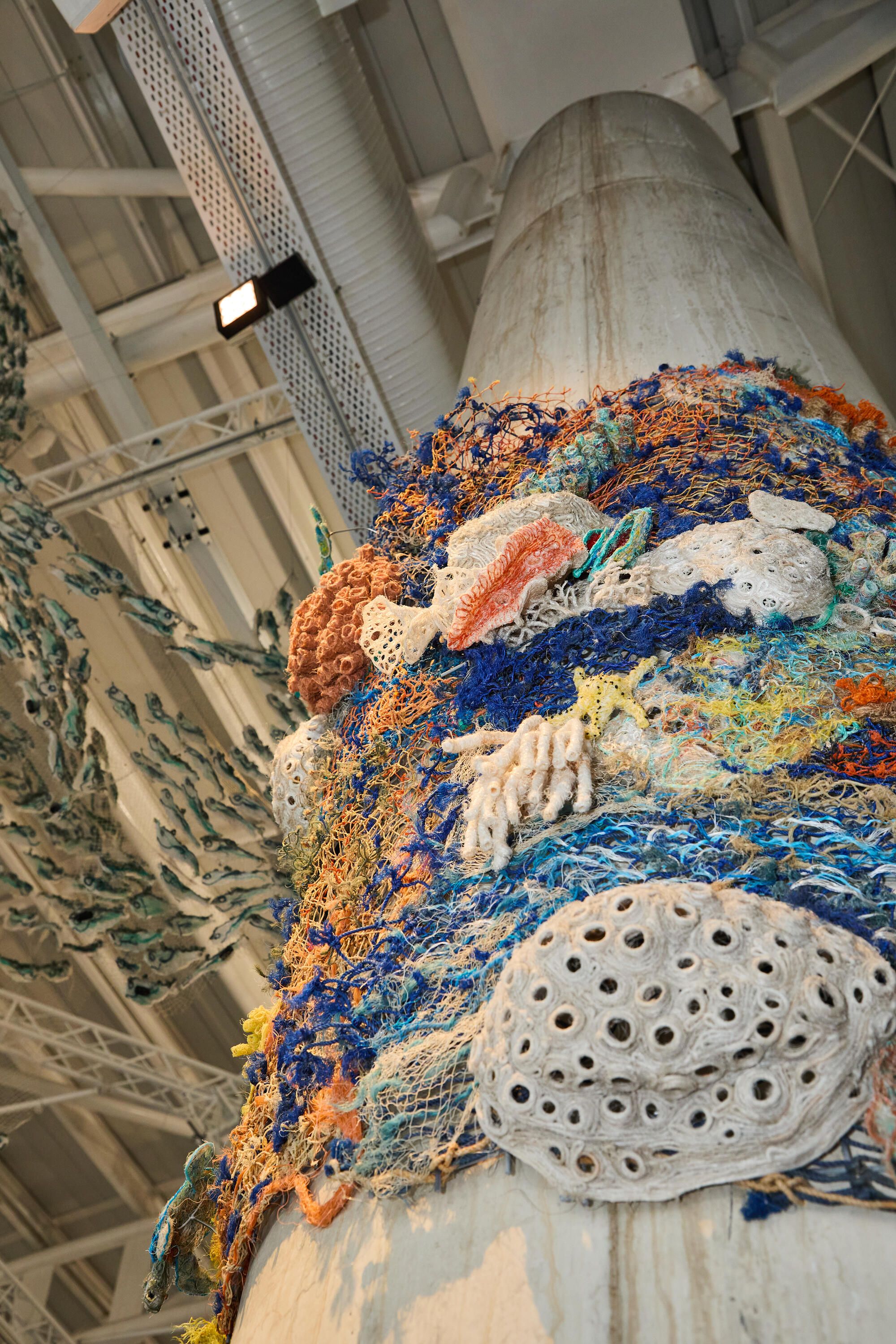 Photo taken looking up at a sculpture which looks like a coral reef and made from recycled plastic twine and nets