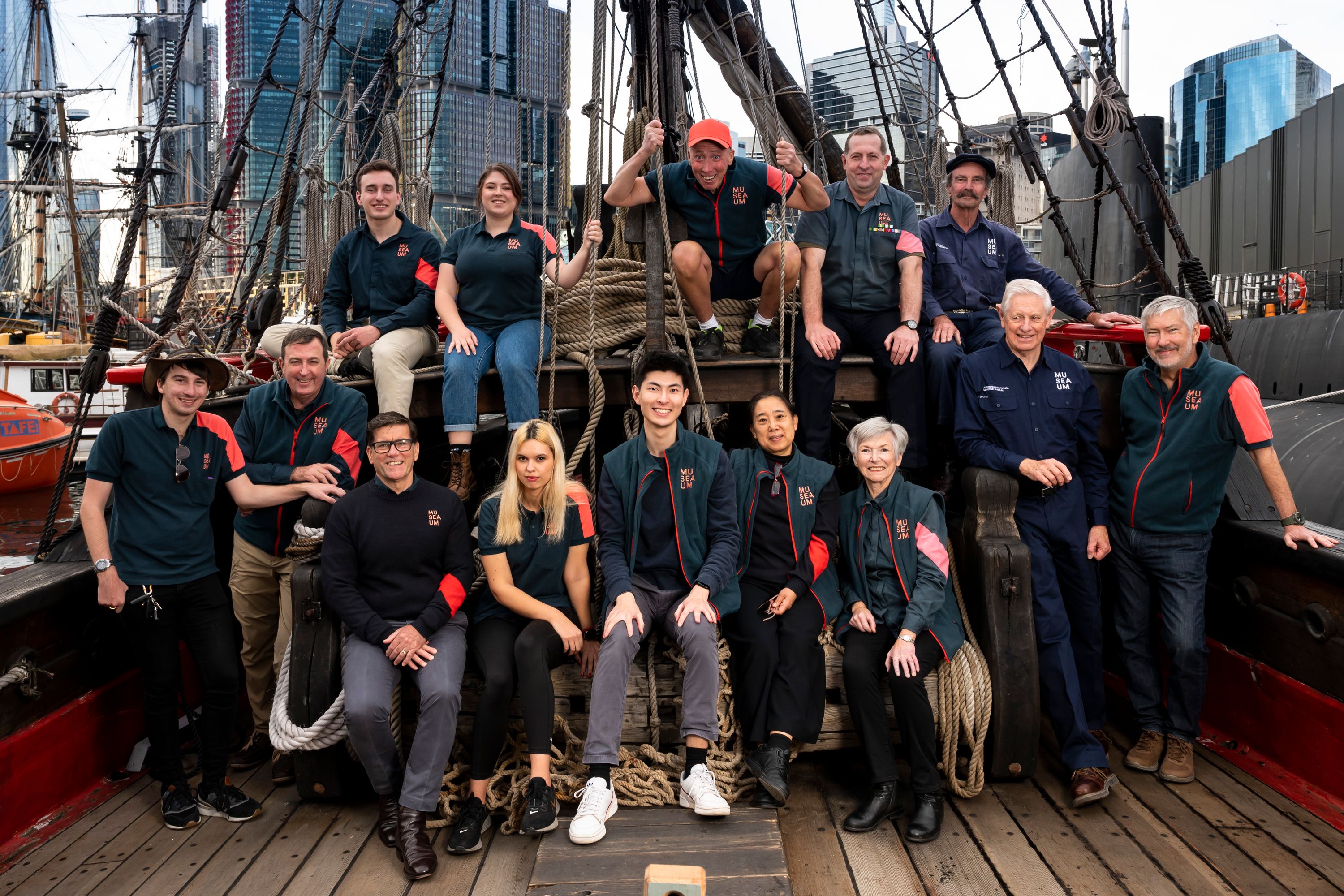 Large group of museum volunteers posing for a photo on the wooden tall ship Duyfken.
