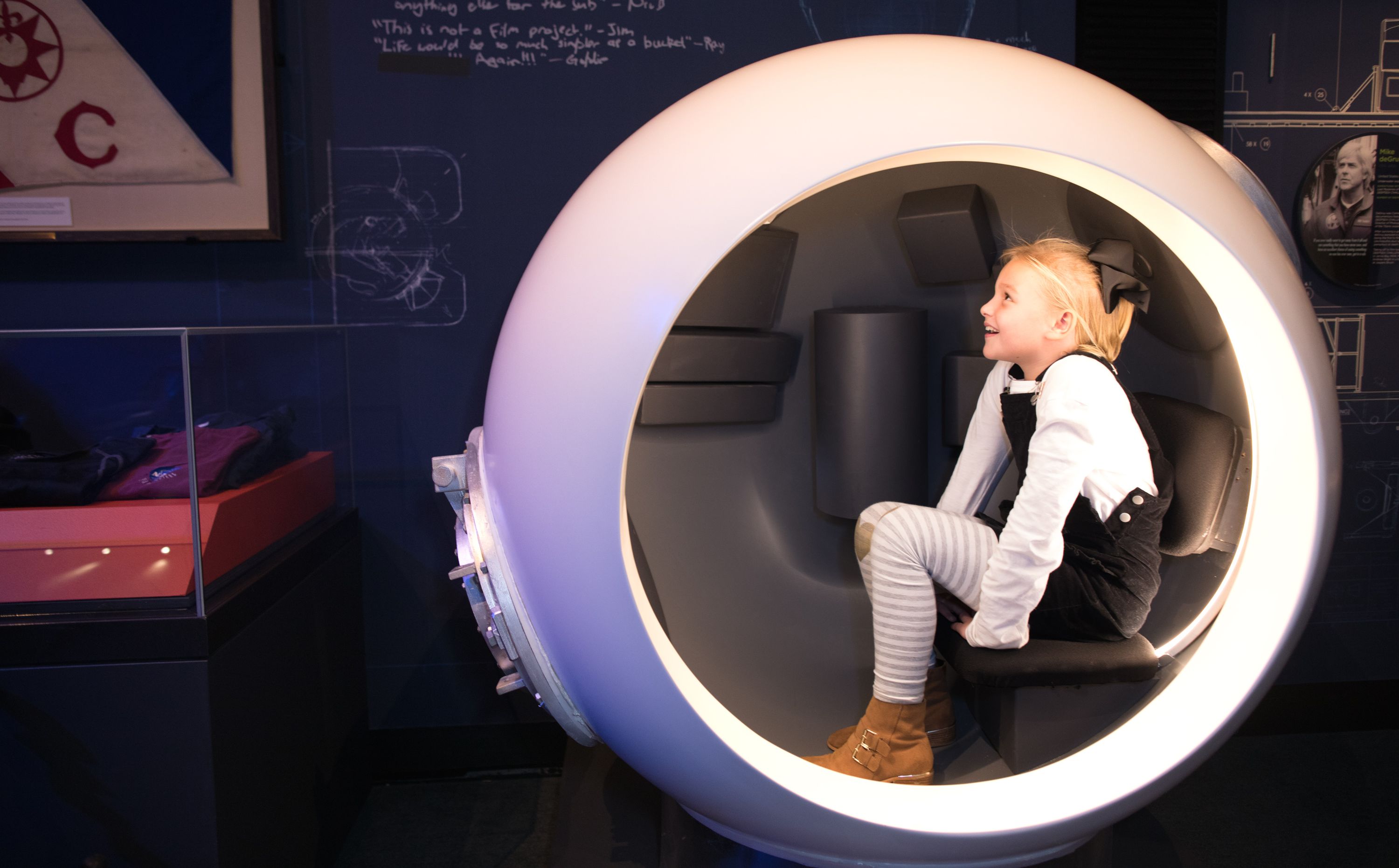 Photo taken inside an exhibition of a girl sitting in a white sphere.