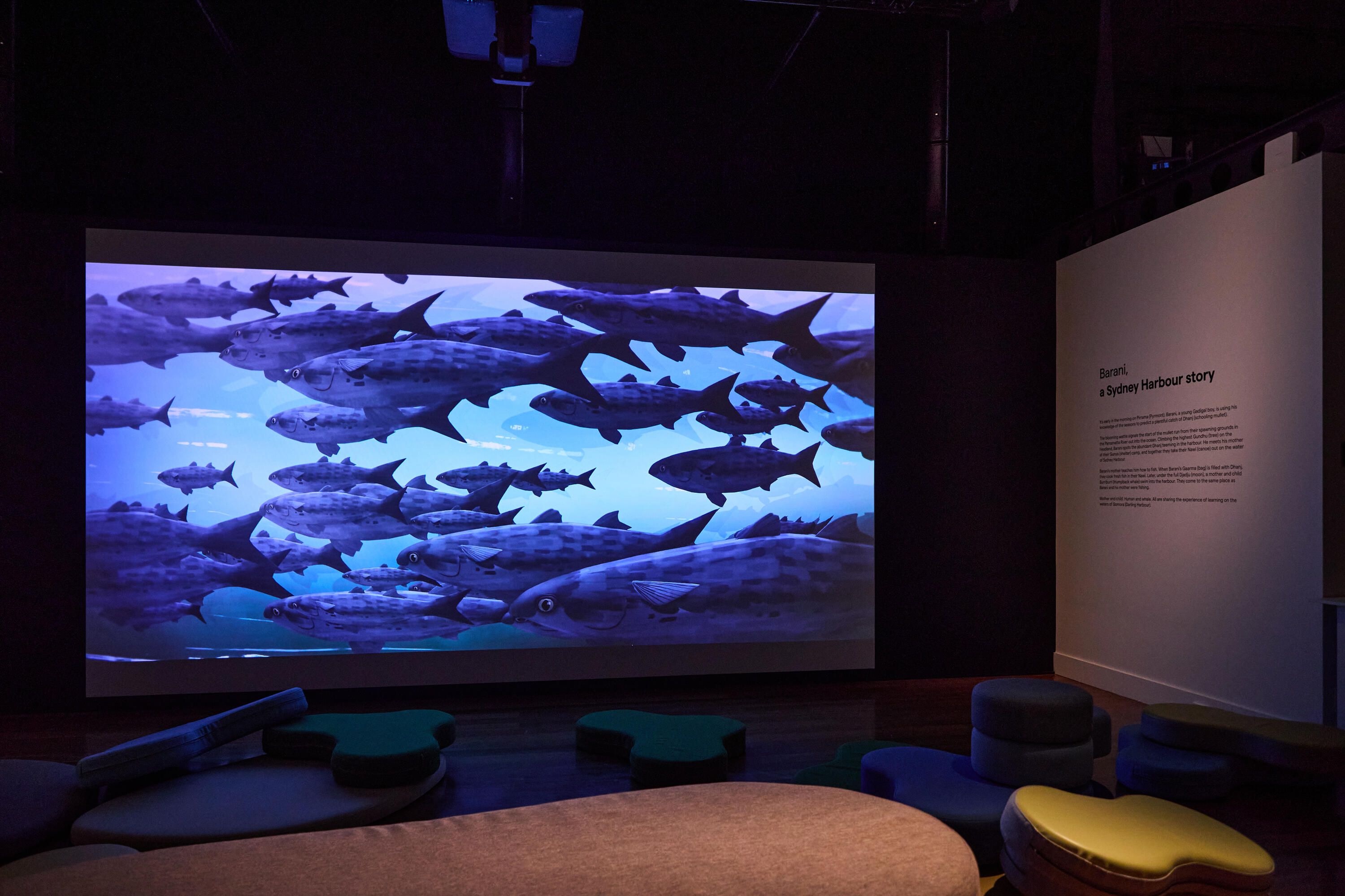 Photo of a museum exhibition space with curved soft seating and a large projection screen