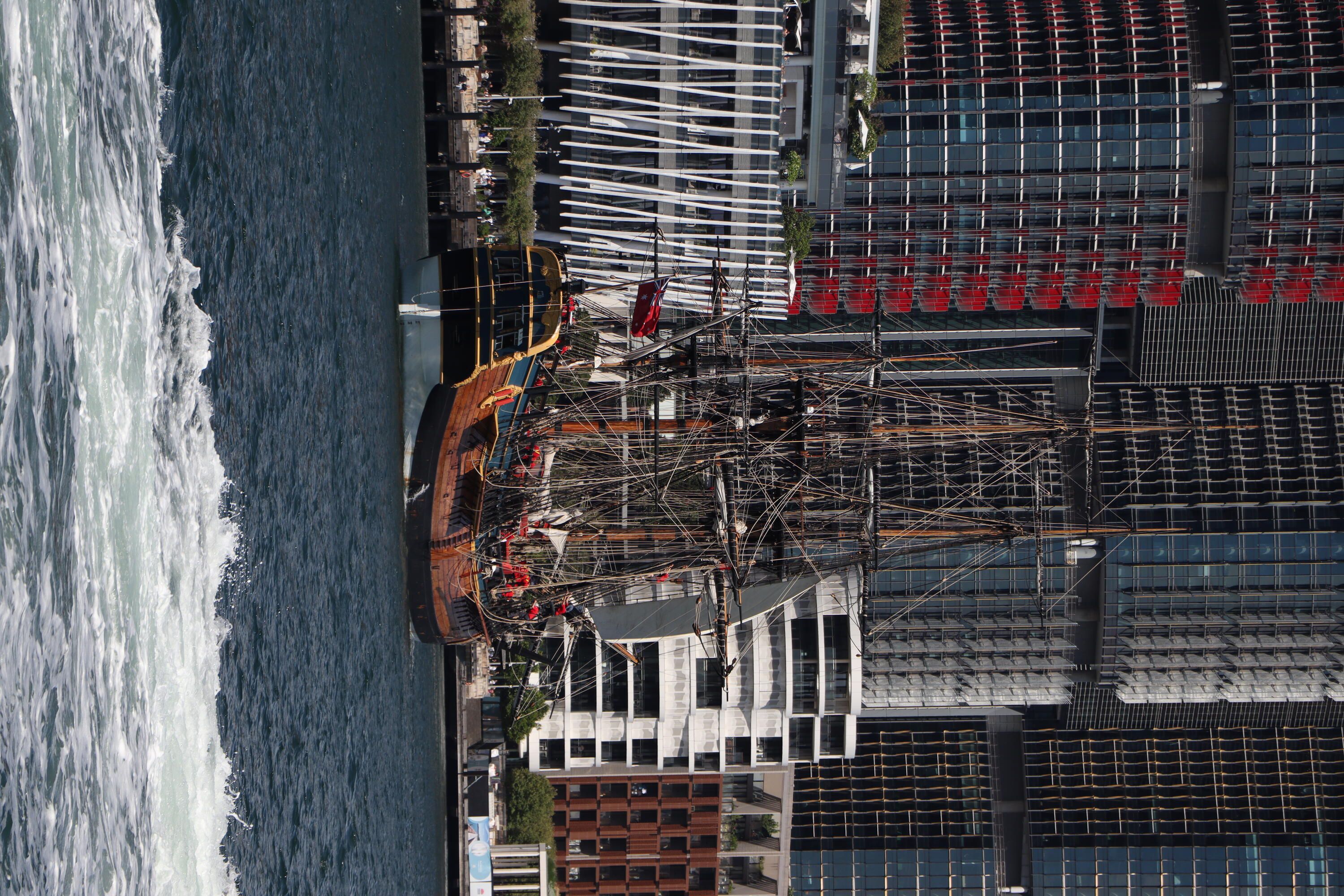 Photo of a tall ship, Endeavour, sailing in the harbour, with tall building behind it. 