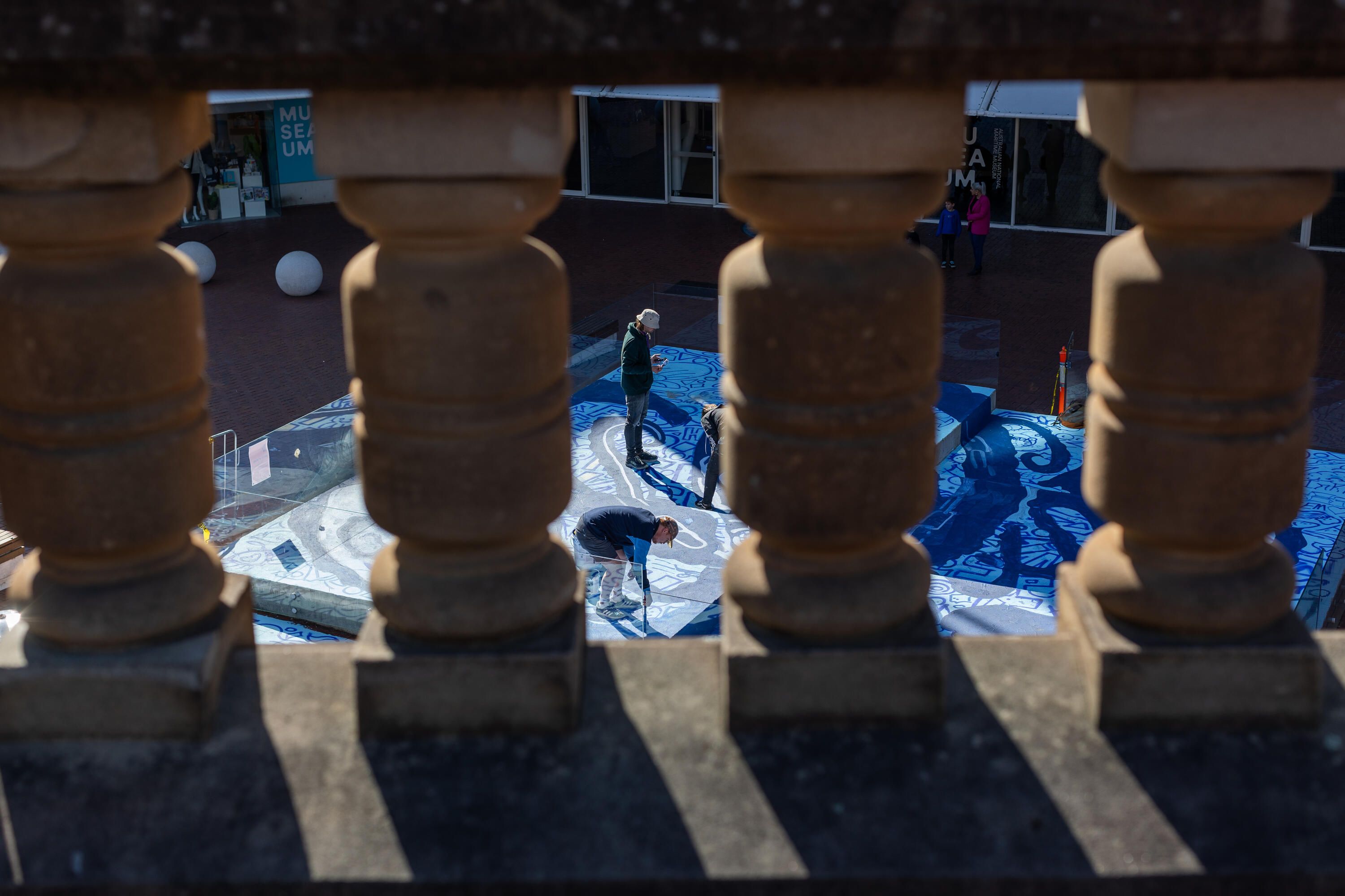 Photo looking through stone pillars at a group of people painting a mural.