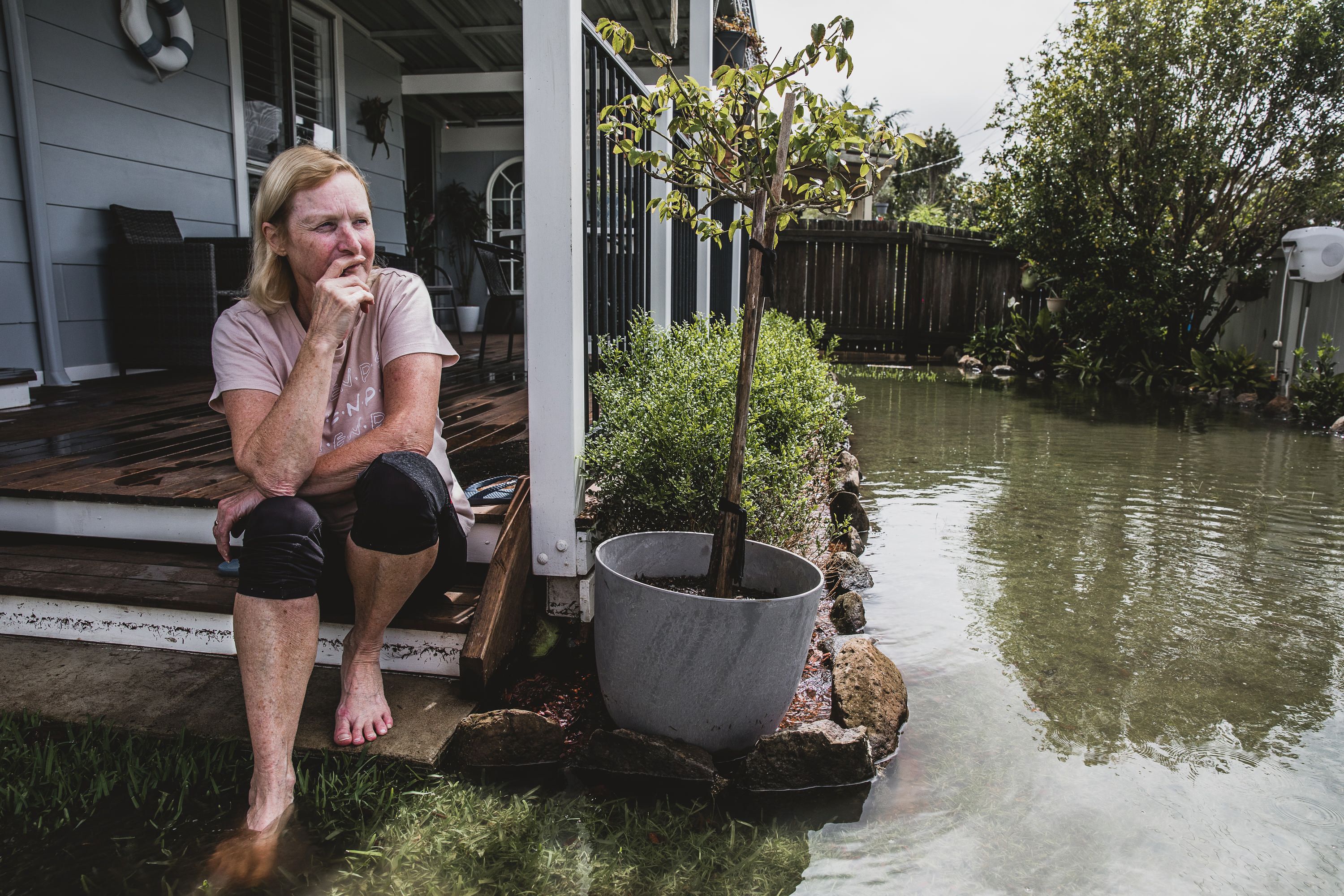 Photo of a woman seated of a verandah looking out over a flooded garden. 