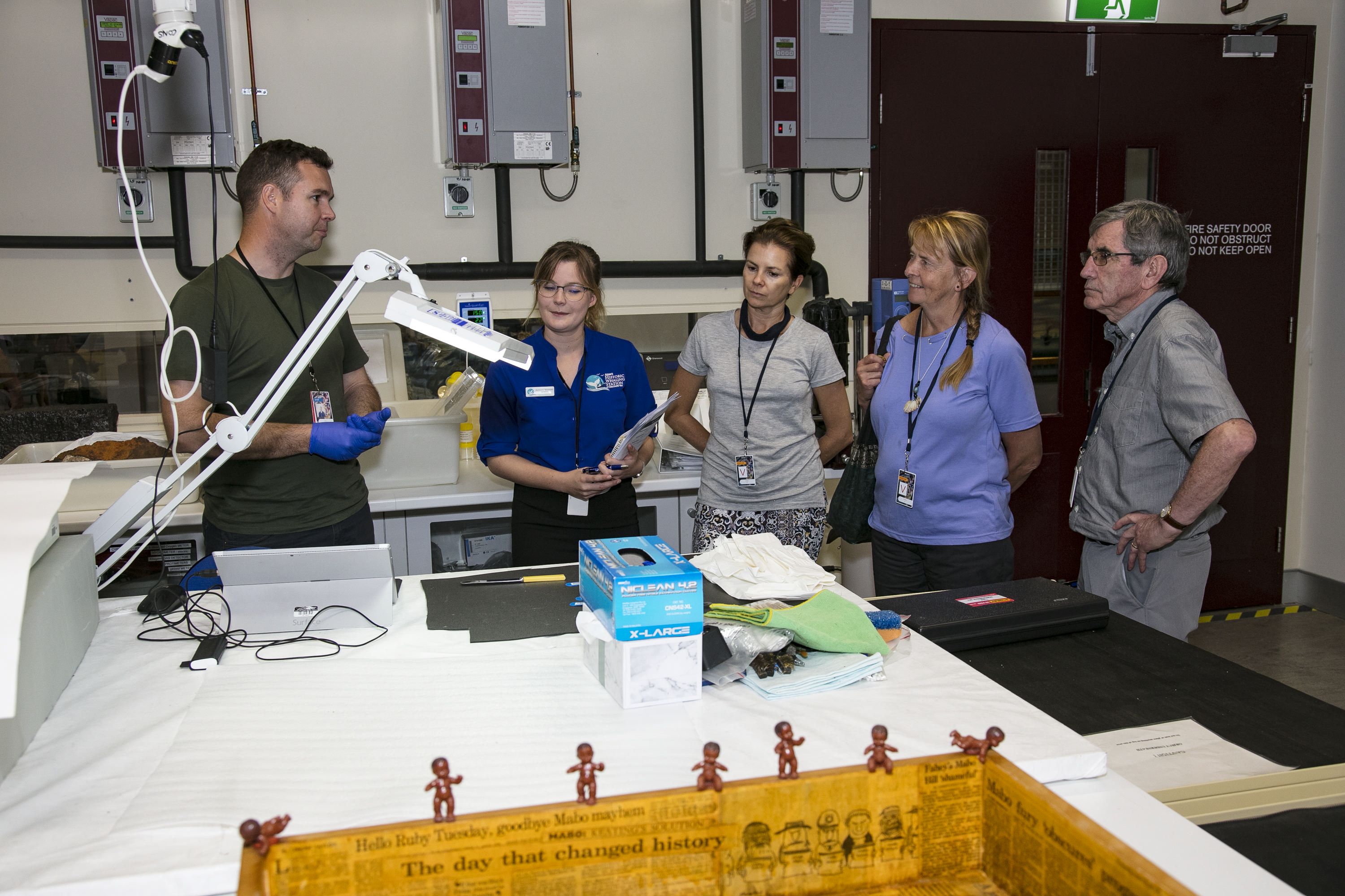 Photo showing 5 people standing around a table in a conservation lab. 