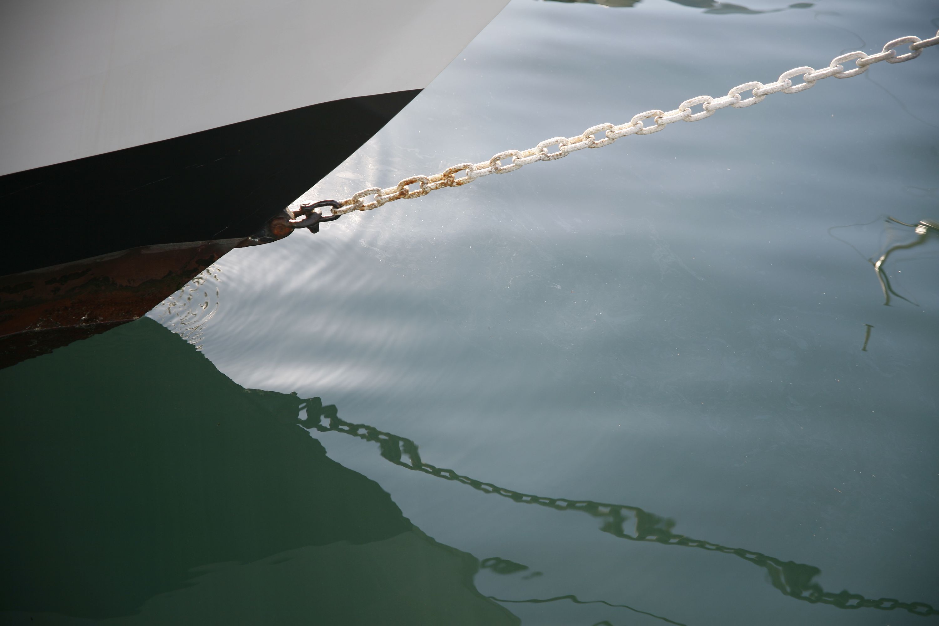 Close up photo showing reflections in the water with a boat's hull in the top left corner. 