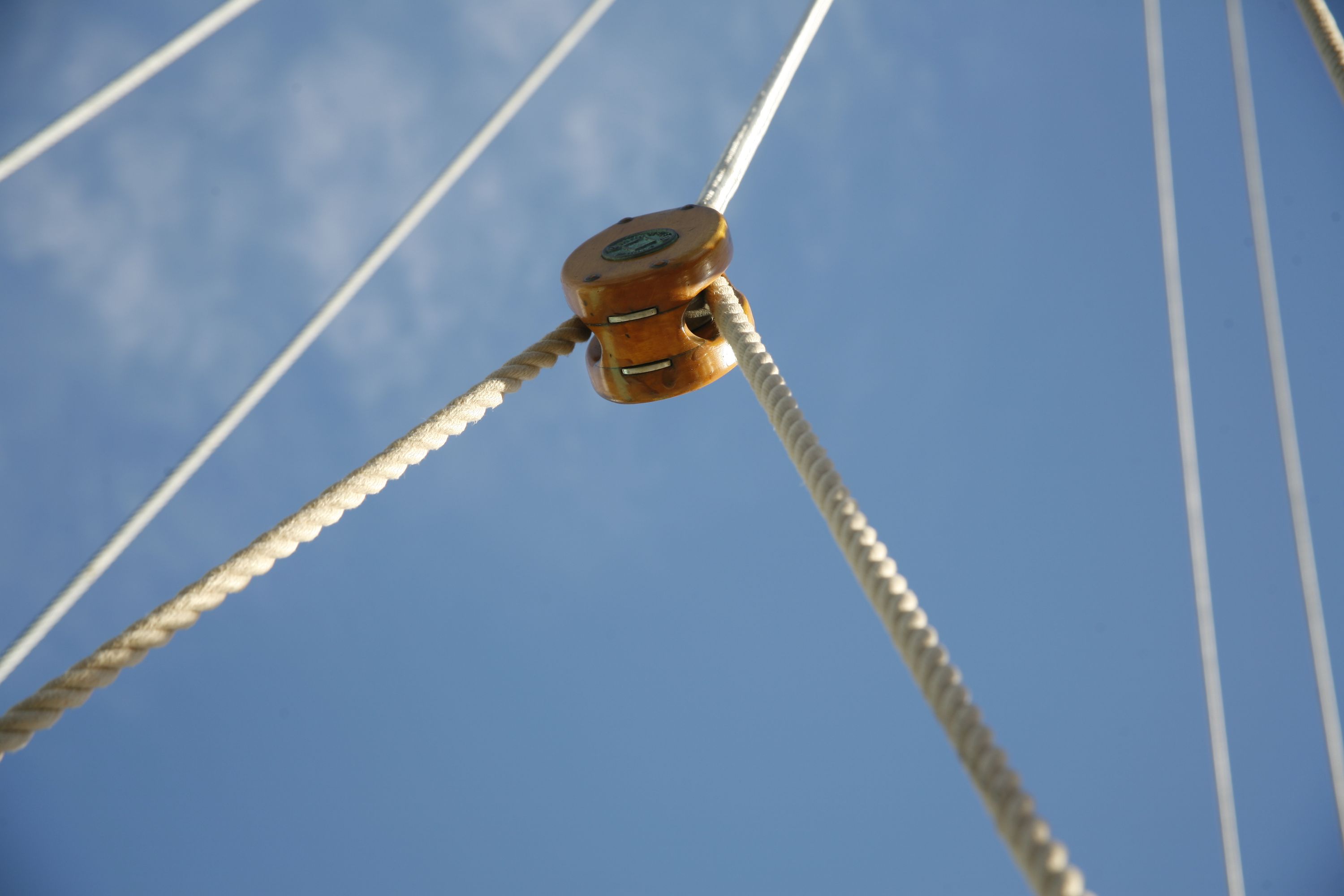 Photo showing a wooden pulley and ropes with a blue sky behind. 