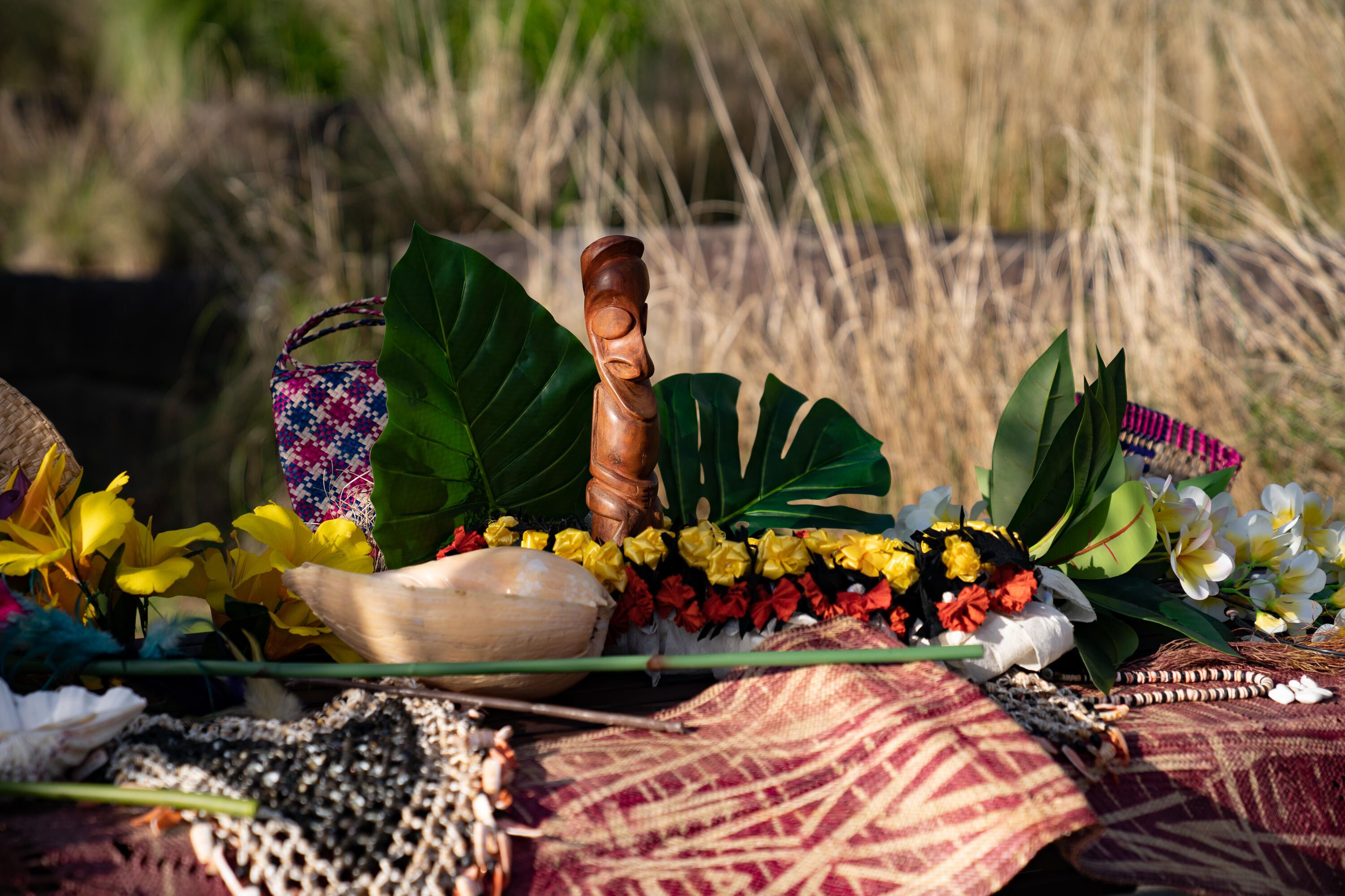 A photo showing a table decorated with flowers and leaves and a wooden sculpture, with grass in the background.
