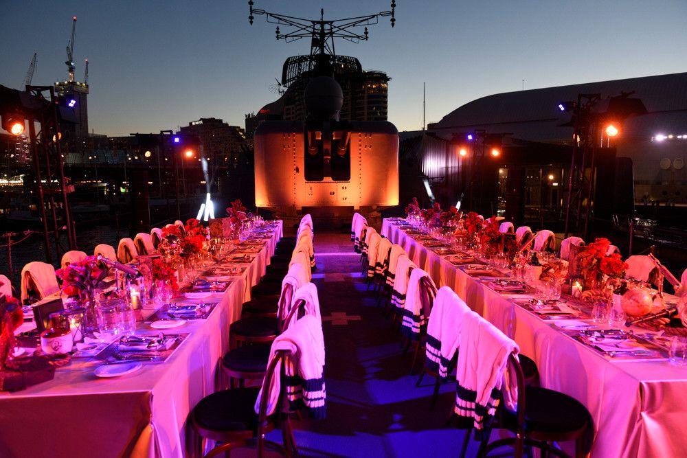 photo of the deck of a navy warship at dusk, with long tables set up for a formal event and intense pink lighting