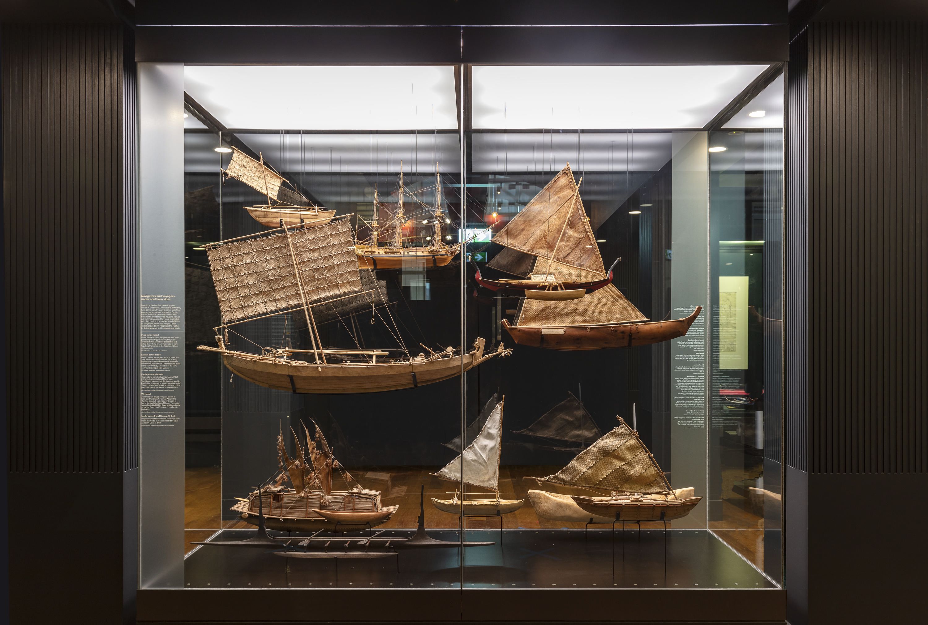 Photo of a display case in a museum exhibition, displaying suspended models of different first nations and pacific watercraft. 