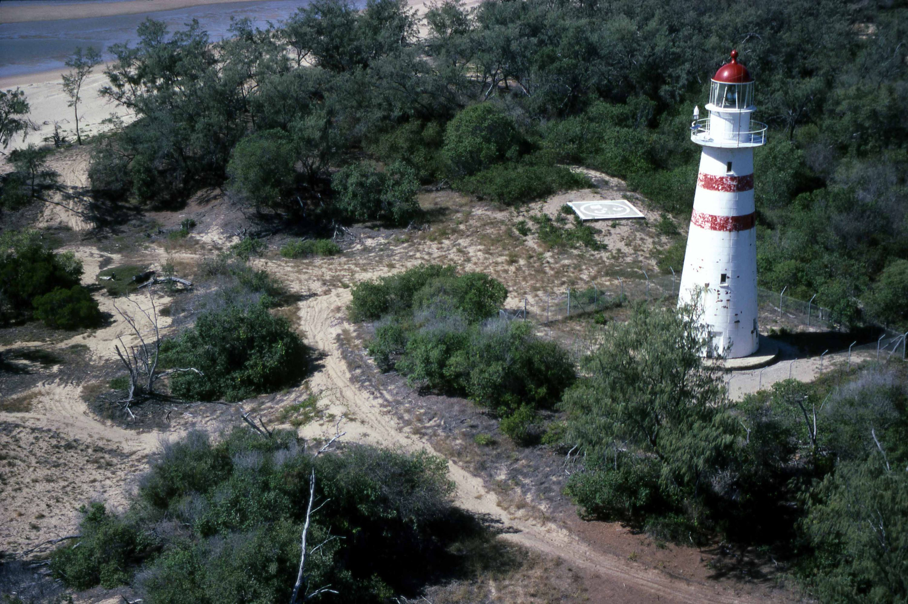 Aerial photograph showing the lighthouse on the right surrounded by scrub with beach visible at upper left.