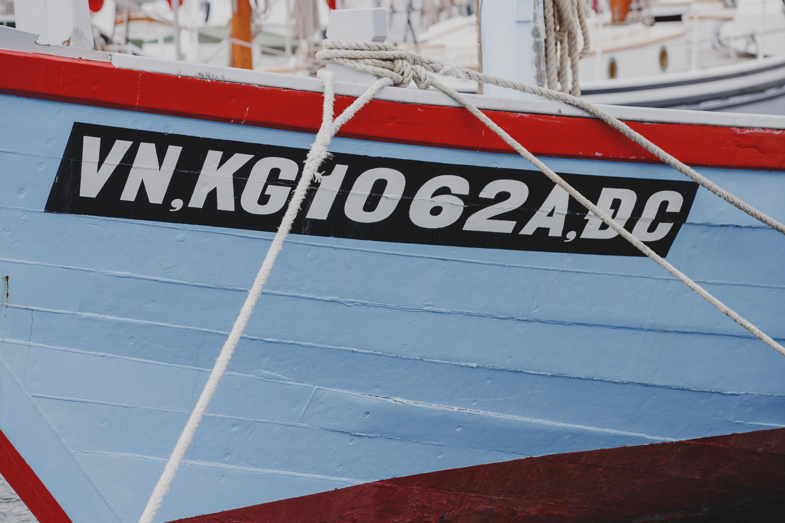 Photo showing a close up of the side of a wooden boat painted blue. It has NV,KG1062A,DC painted on its side