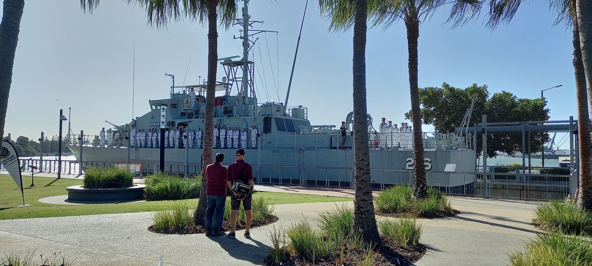 Photo of a large navy vessel behind 3 tall palm trees.