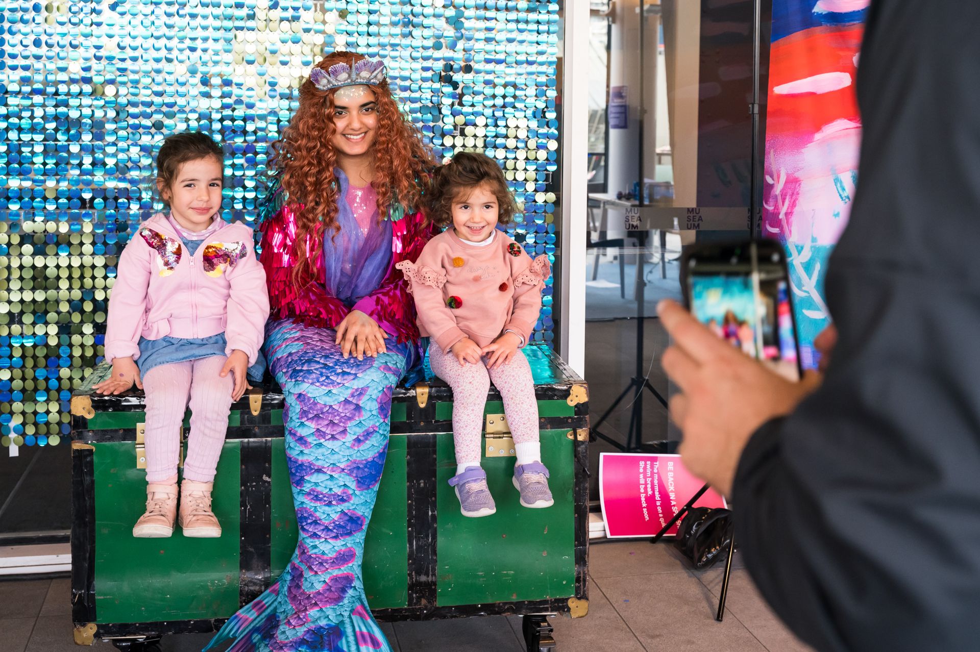 Photo of a woman in a mermaid costume having a photo taken with 2 young girls