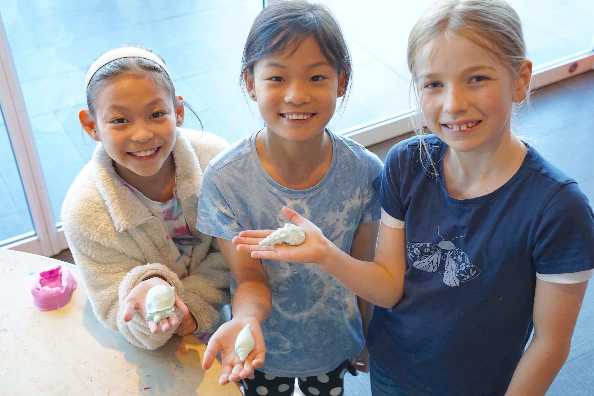 3 girls holding their artworks which look like shells 
