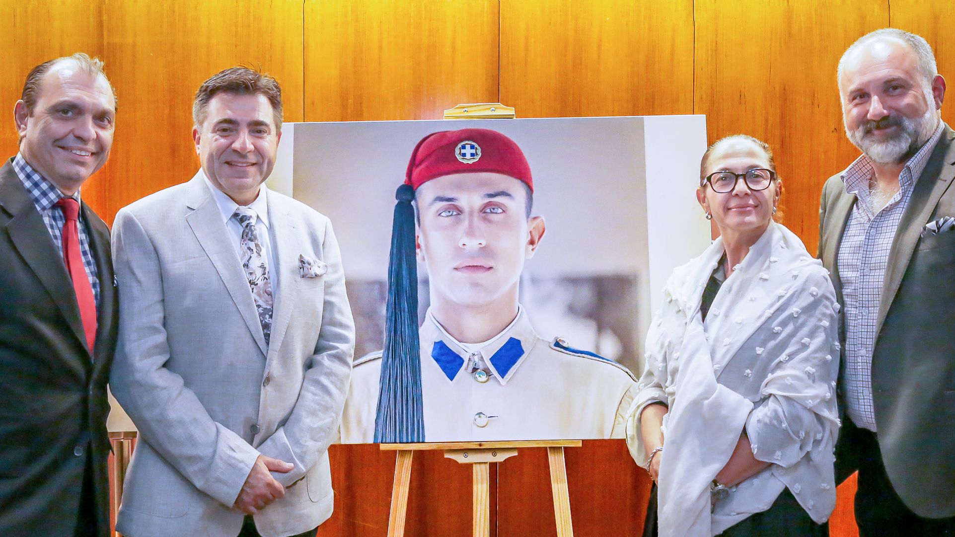 Photo of 4 people, 3 men and 1 woman, standing either side of a large portrait of a man.