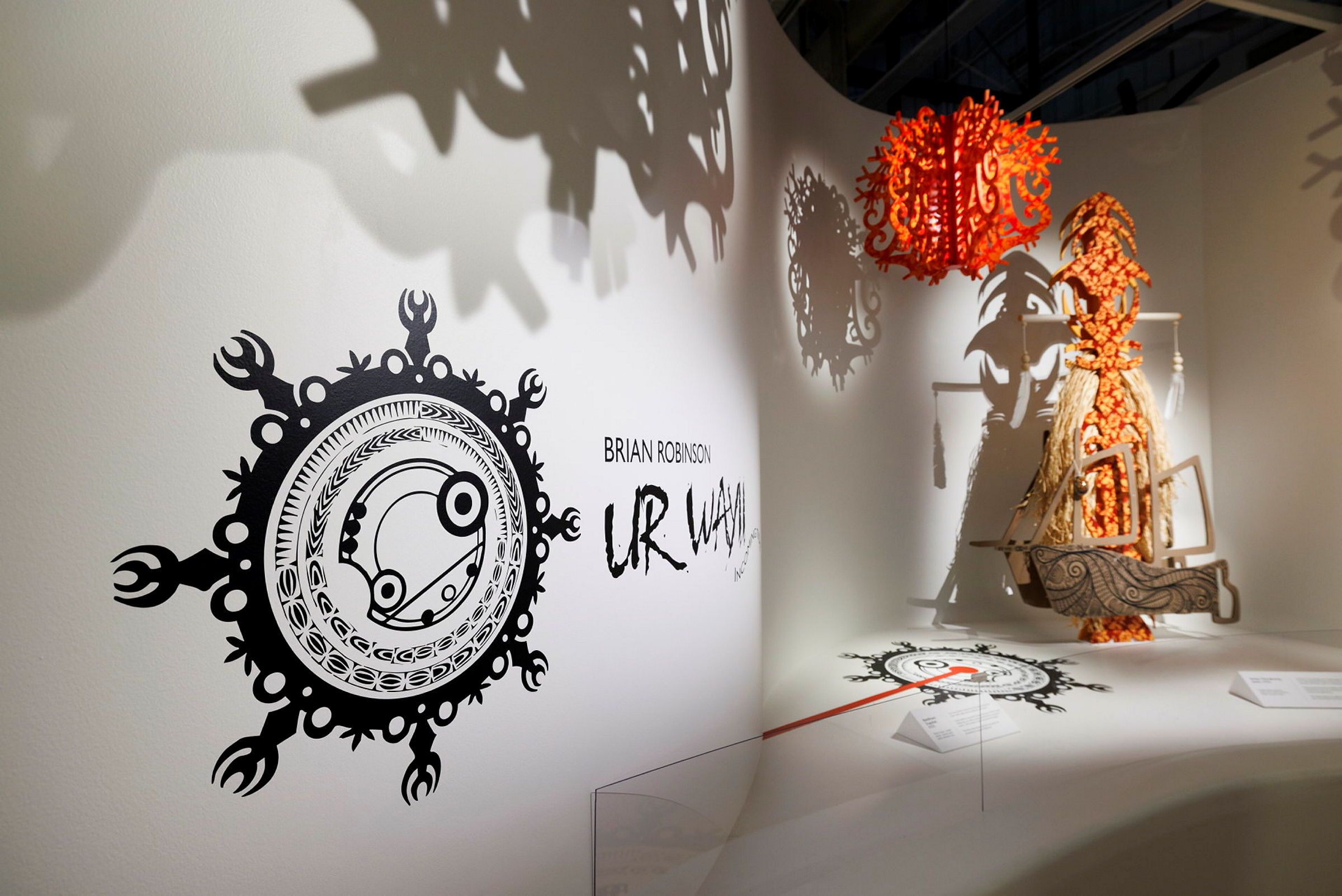 Photo of a museum exhibition space, with sculptures on a plinth and hanging from the ceiling.