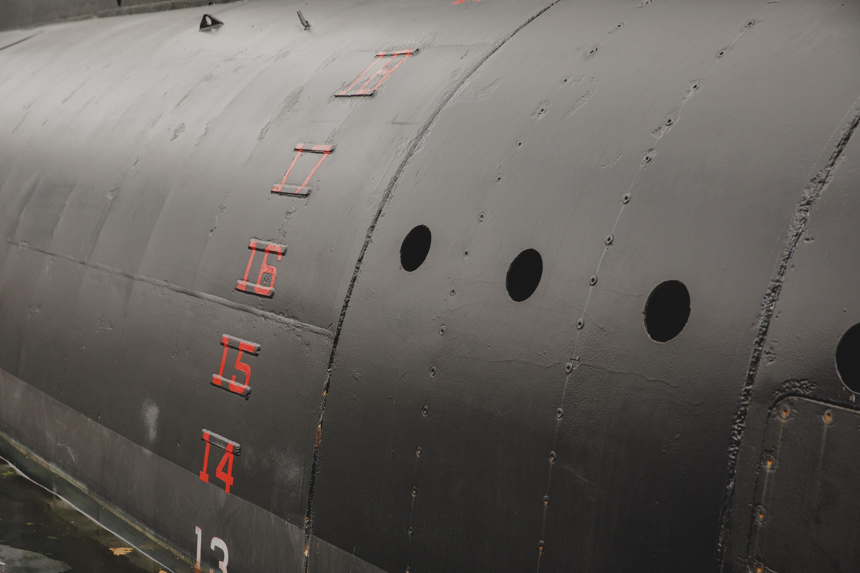 Close up photo of the curved outside hull of a submarine, with red numbers in a vertical line. 