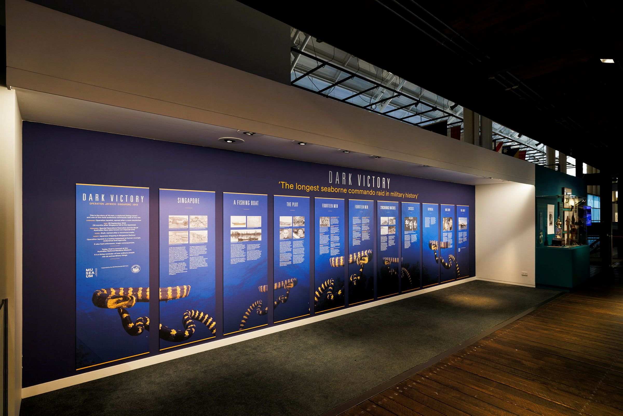 Photo showing a museum exhibition, with text and images on printed panels along a wall.