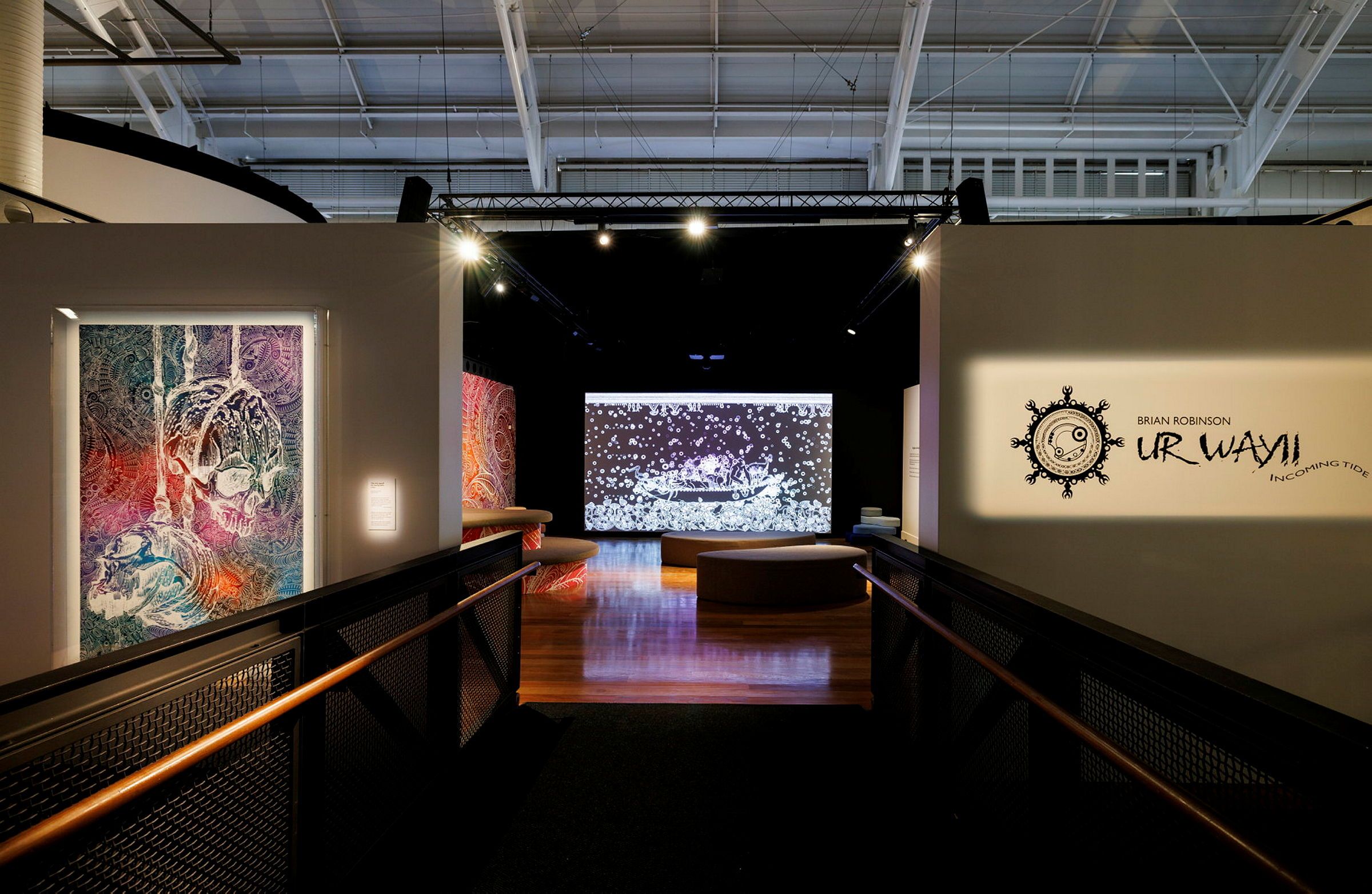 Photograph looking through a doorway at a large screen, with an artwork and exhibition text on the wall by the door.