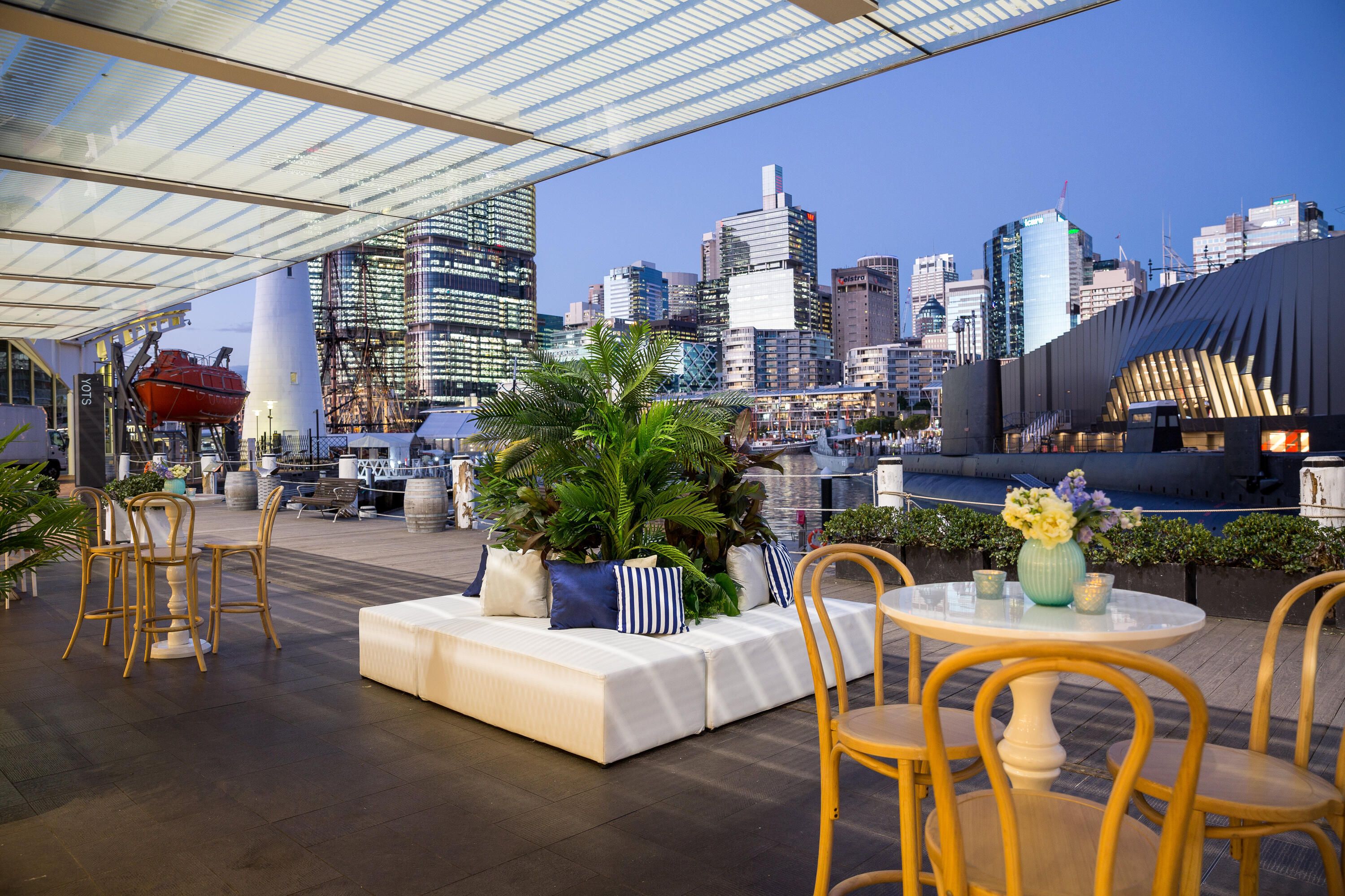 Photo of event, outdoor furniture and plants with the Sydney skyline at dusk in the background.