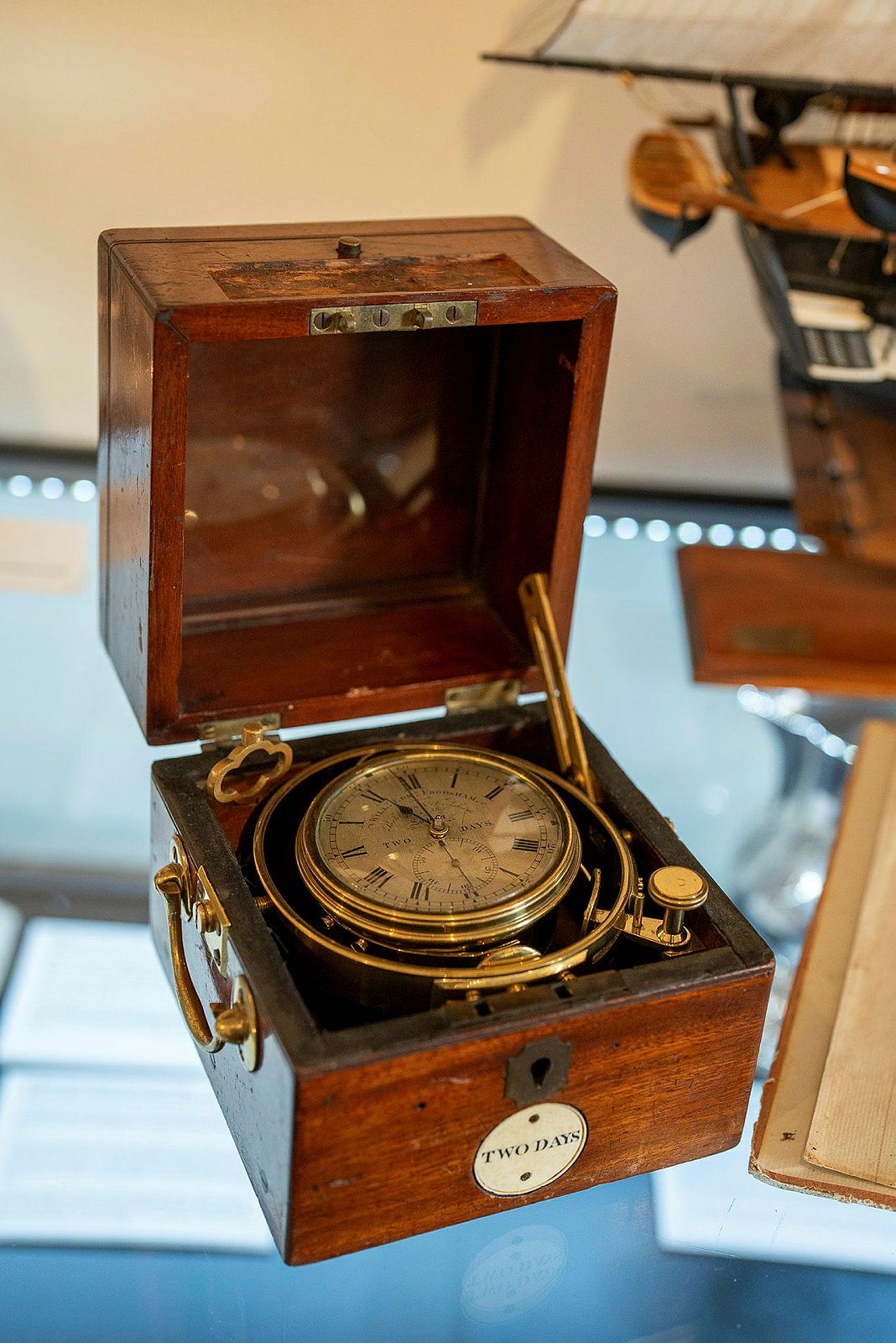 Photograph showing a marine chronometer (clock) in a wooden case.
