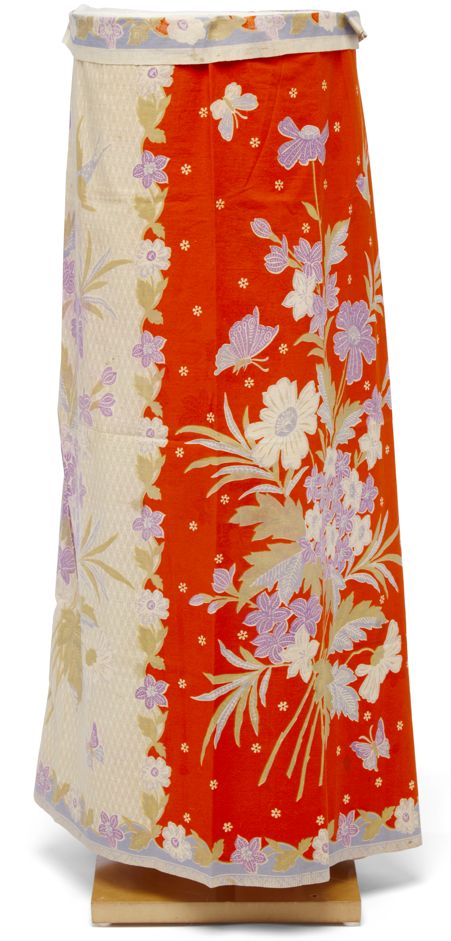 Orange ad cream sarong with pastel flowers. It is on a wooden stand. 