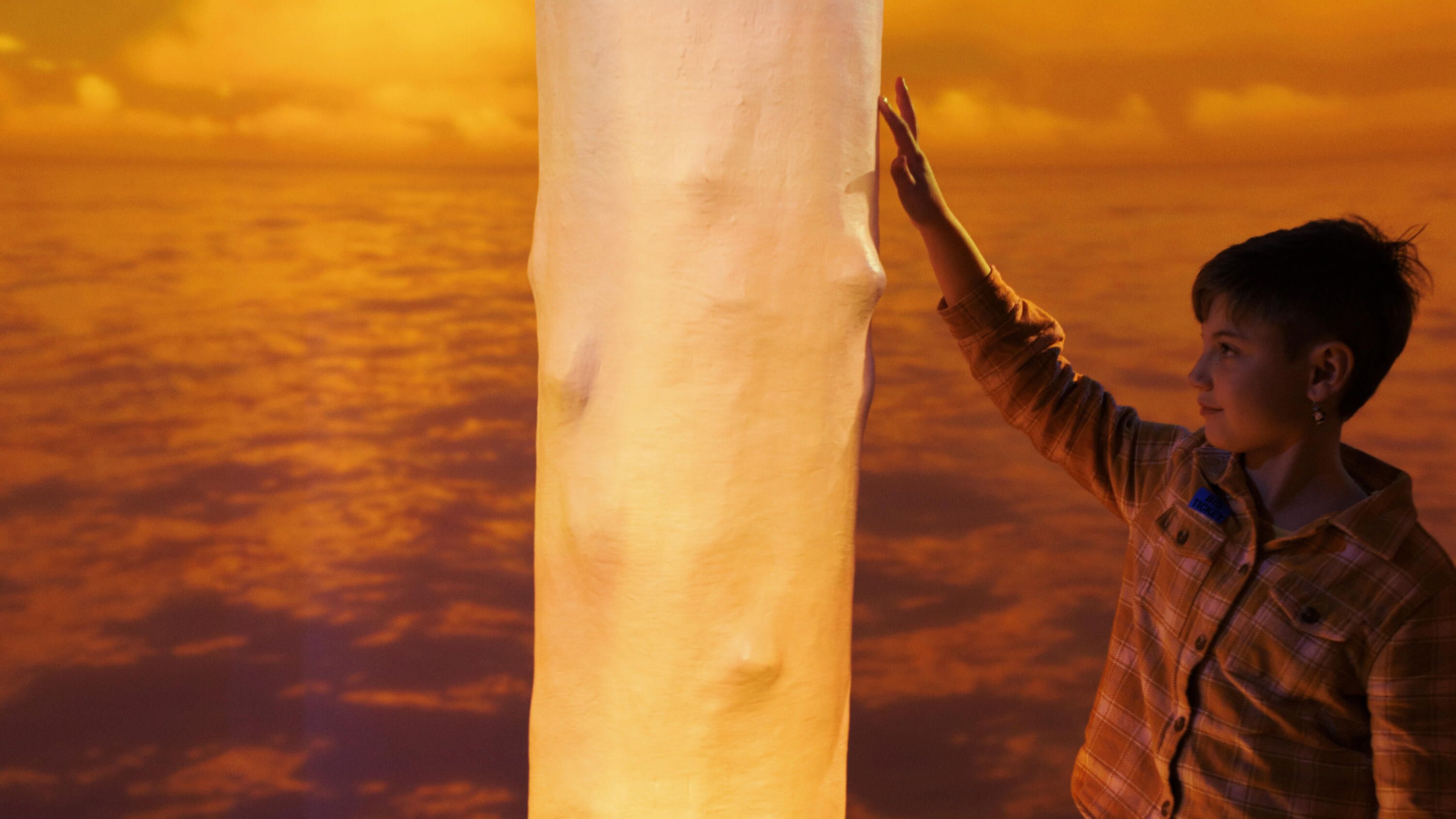 Boy touching a wooden pole, with a glowing orange projection on the pole and in the background.