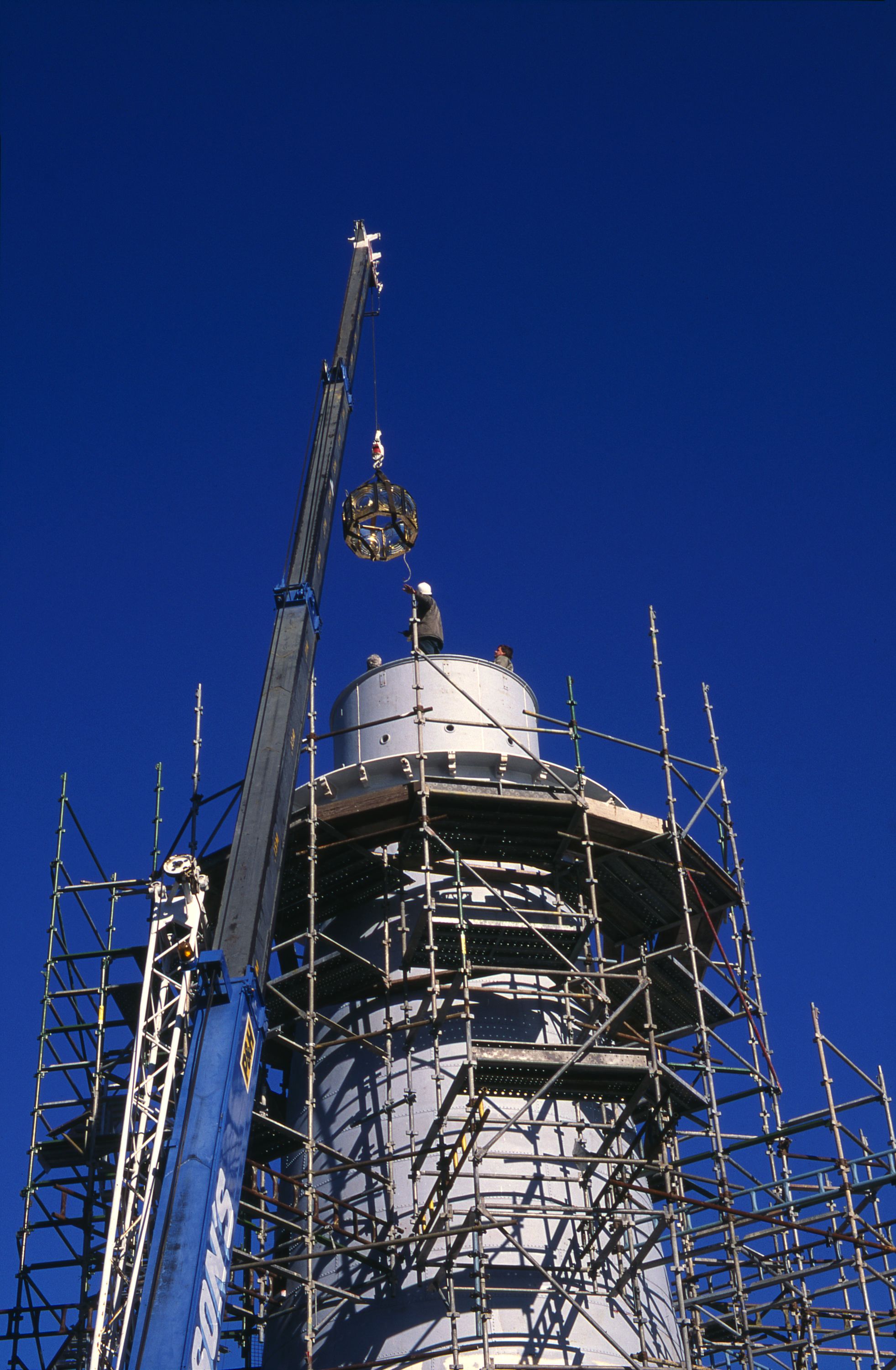 Photo showing the top of a lighthouse being reconstructed, surrounded by scaffolding. 