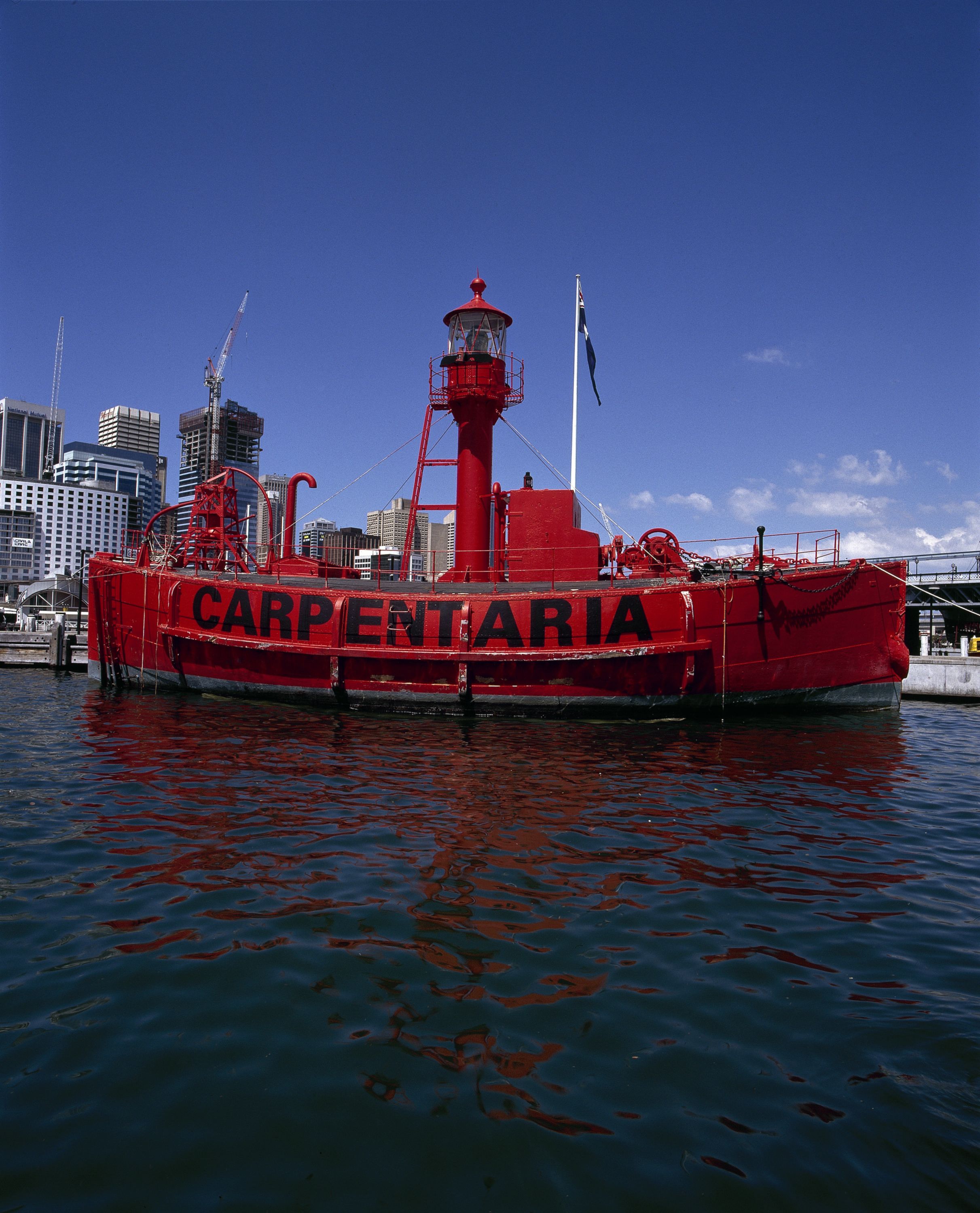 Photograph of a red lighthouse ship, with the name CARPENTARIA in black along the side on the water. 