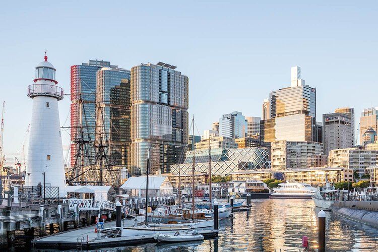 Photo taken of darling harbour showing boats and a lighthouse, with buildings in the background. 
