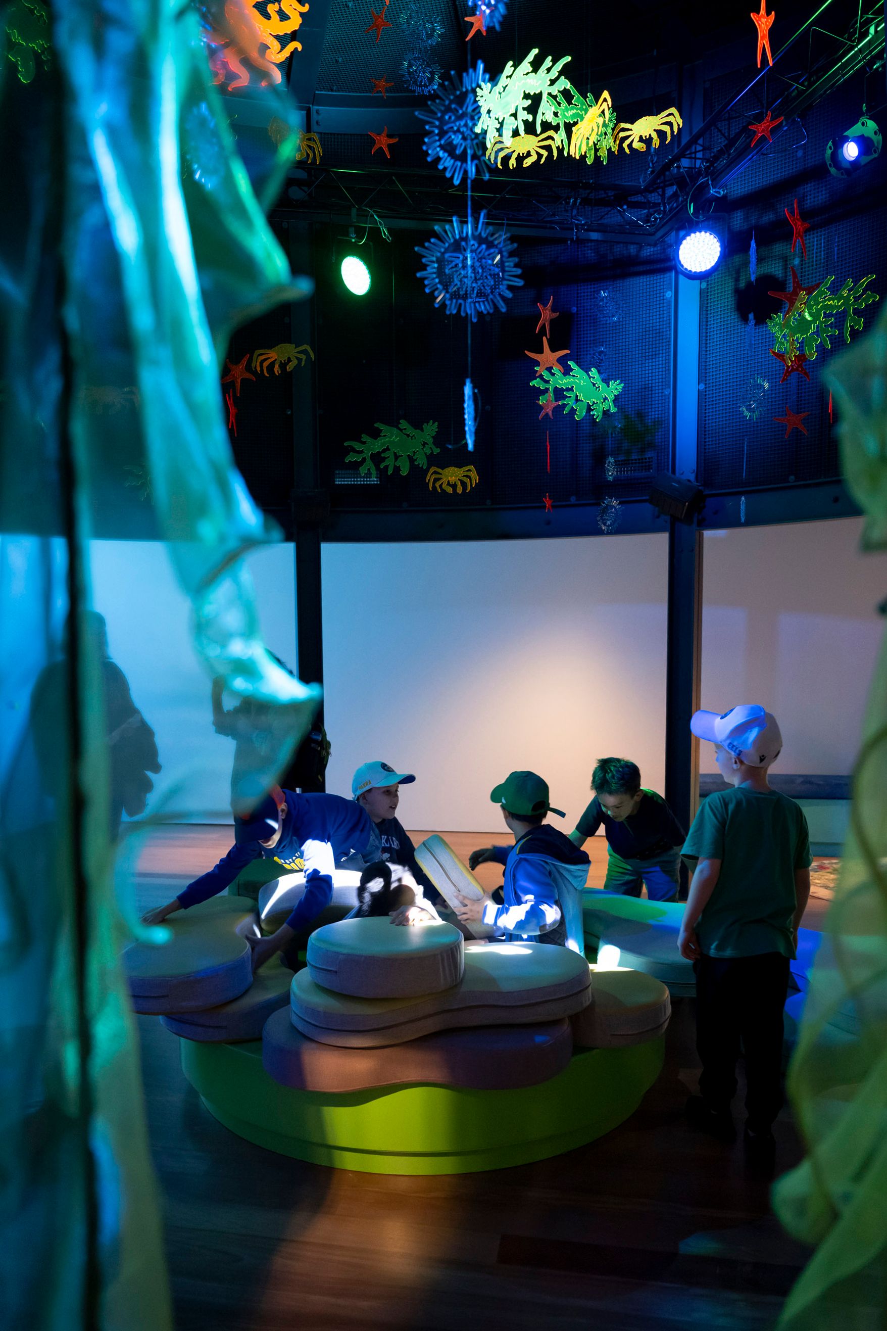 Photo showing a dim, calm space with children seated on soft floor cushions and. sea themed decorations around them.