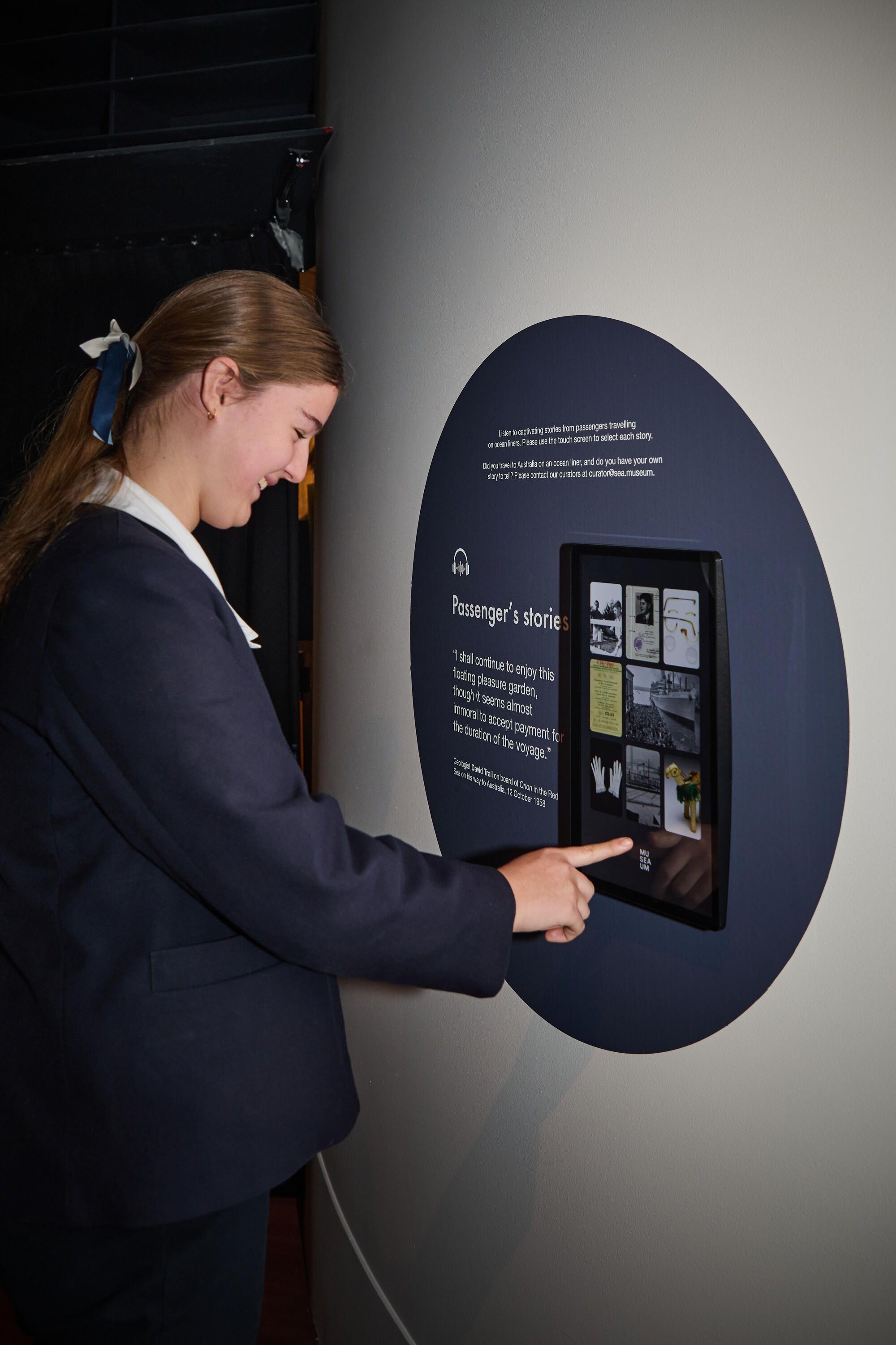 Photo showing a female school student in a navy coloured uniform using a touchscreen in a museum exhibition.