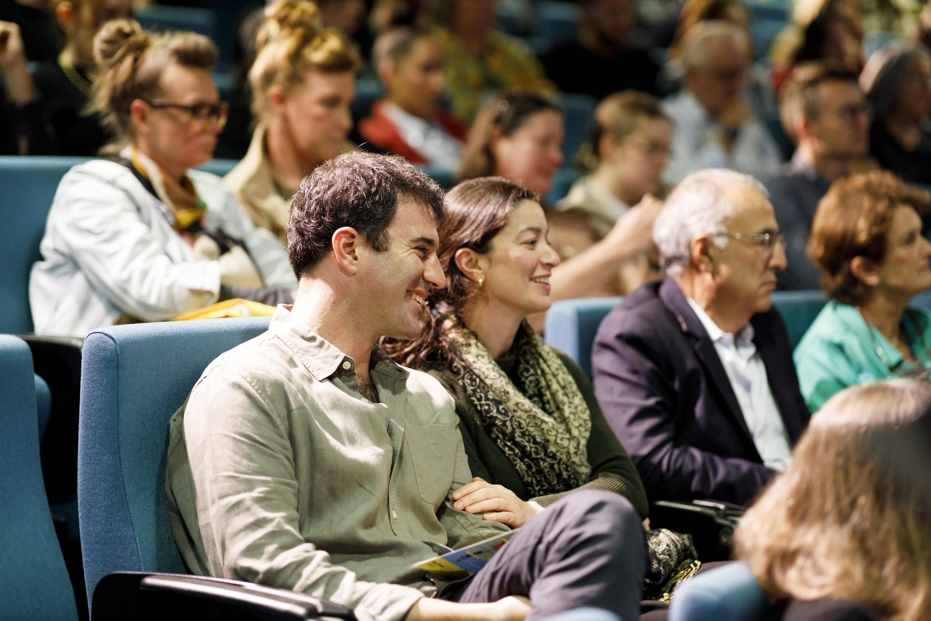 Photo of people smiling while sitting in a theatre. 