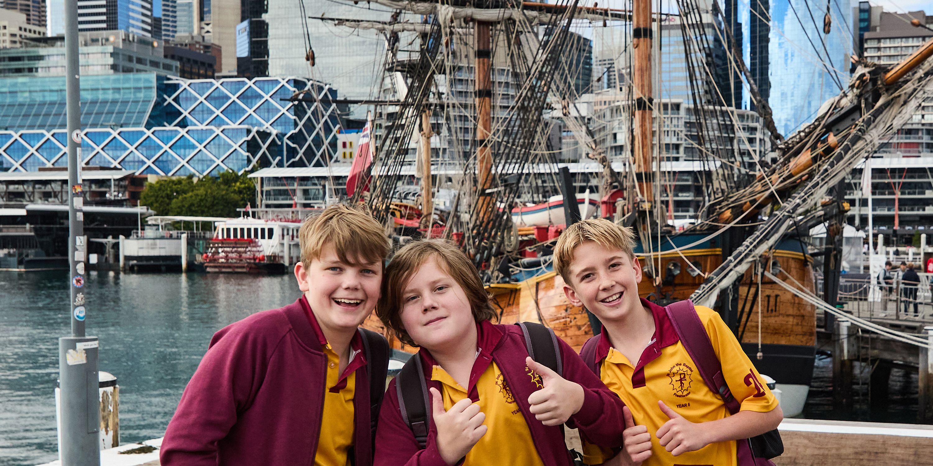 Photo of a group of 3 boys in schol uniforms, with the tall ship Endeavour behind them.