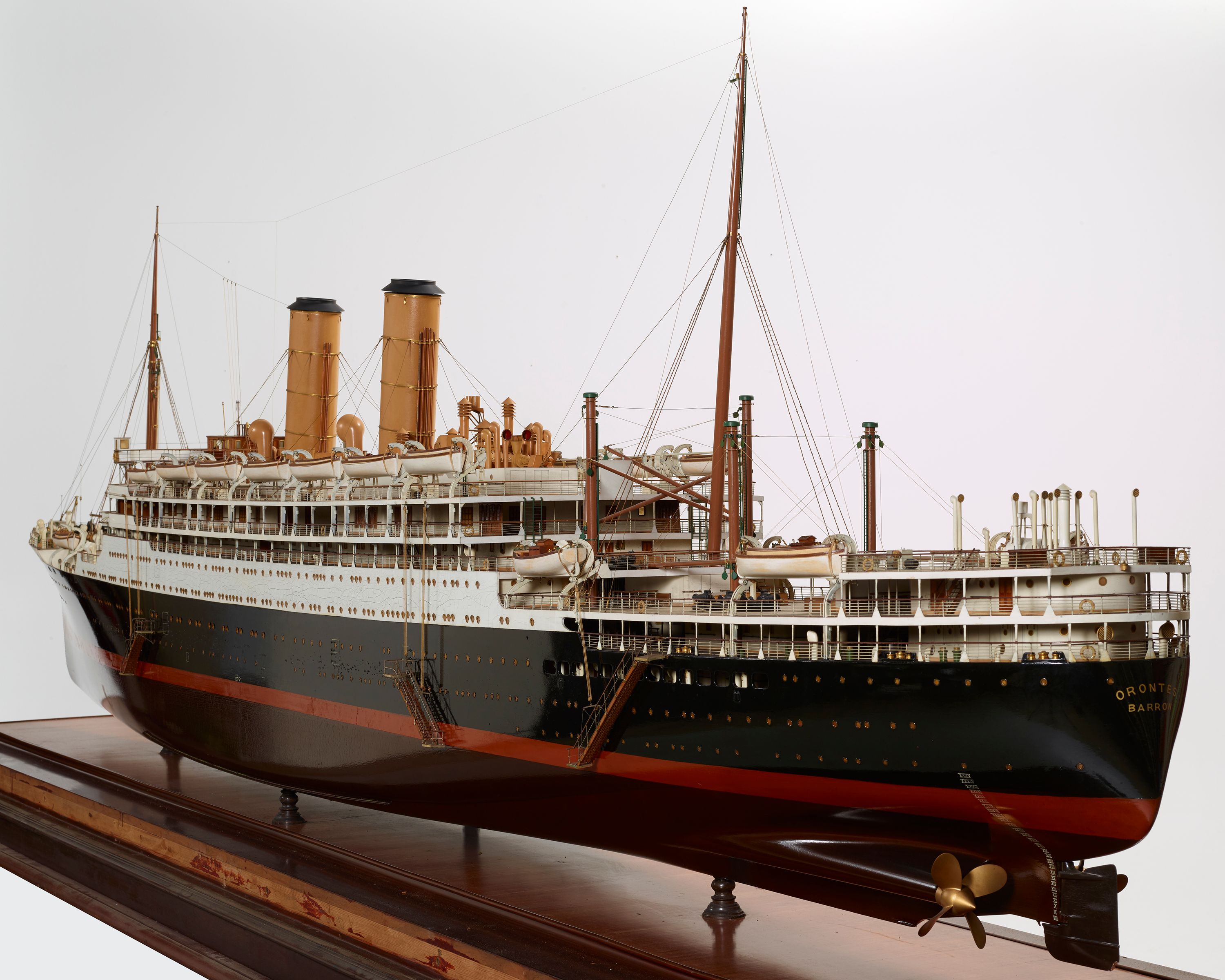 Model of an ocean liner with a wooden black hull, white superstructure, red boot topping, brown anti-fouling and to cream coloured funnels. The mast forward and the mast aft are brown, with six derricks aft complete with winches and rigging. It has ten lifeboats stationed on each side, three boarding (accommodation) ladders on each side, a swimming pool and three hatches on the main deck, aft. Three hatches on the main deck forward, windlass and anchors on the forecastle deck.