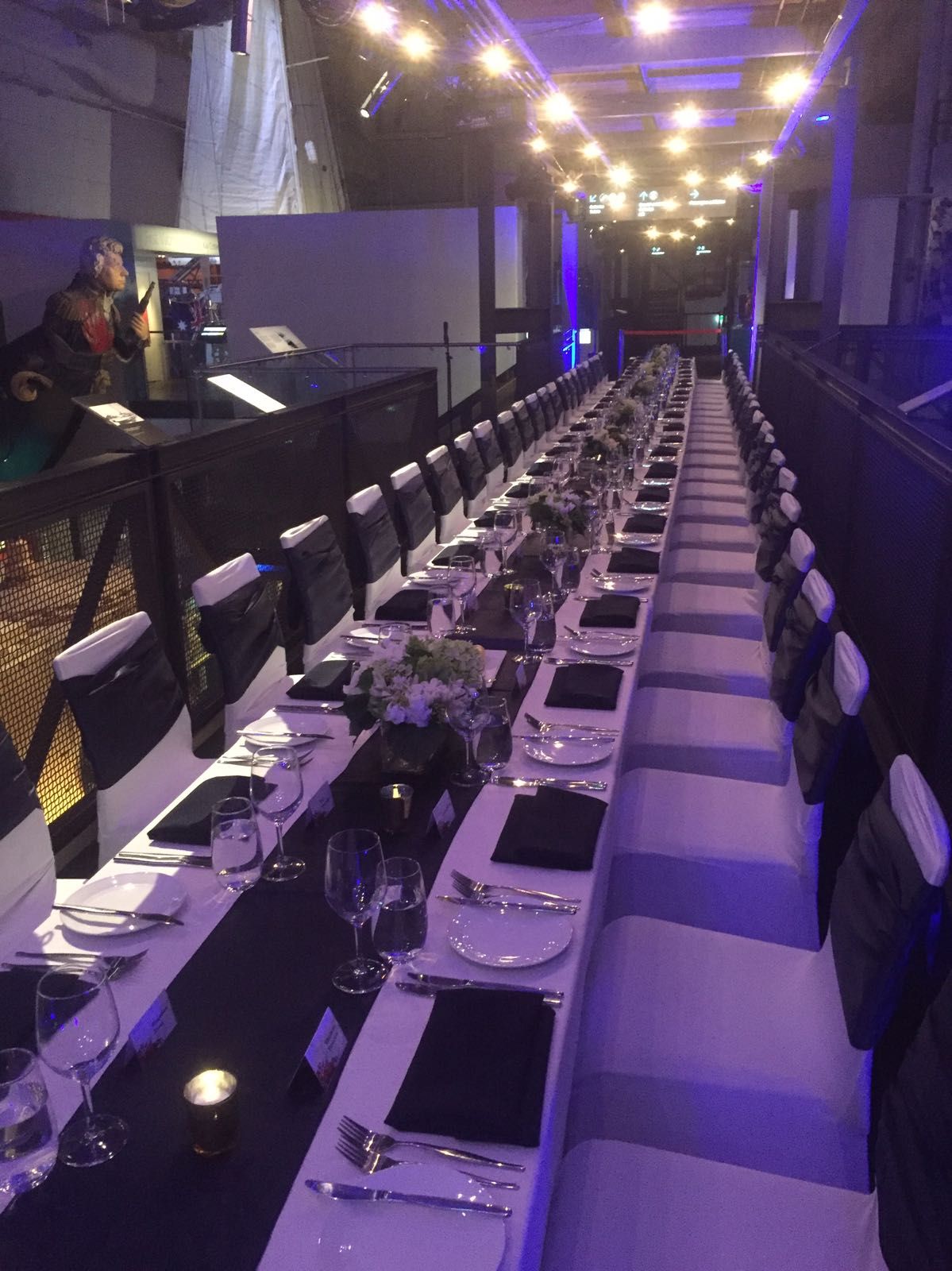 photo of a long table set for a formal event with dim purple lighting.