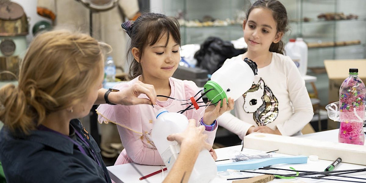 Photo of 2 children (girls) and a woman working on a contraption made from recycled materials