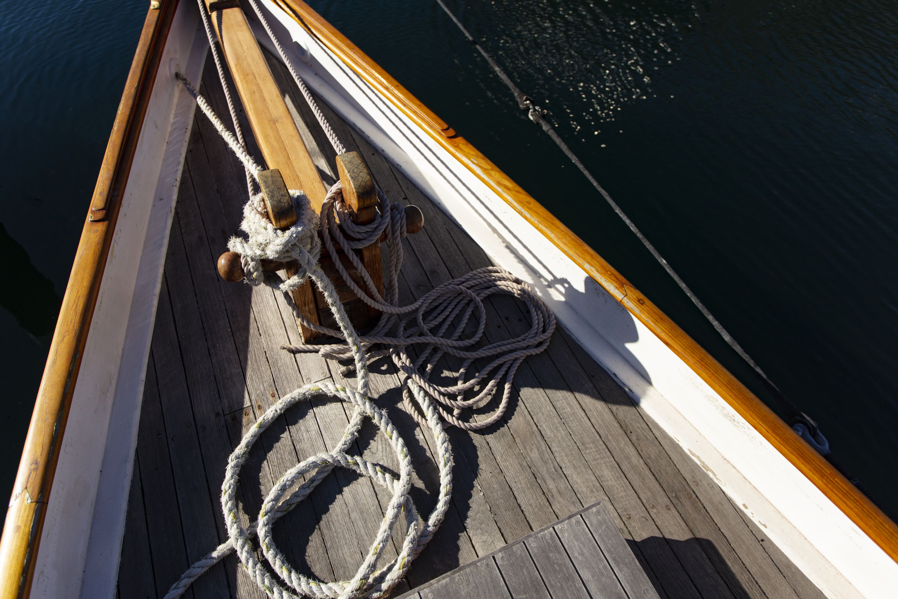 Photo looking down at a the wooden deck of a vessel with ropes.