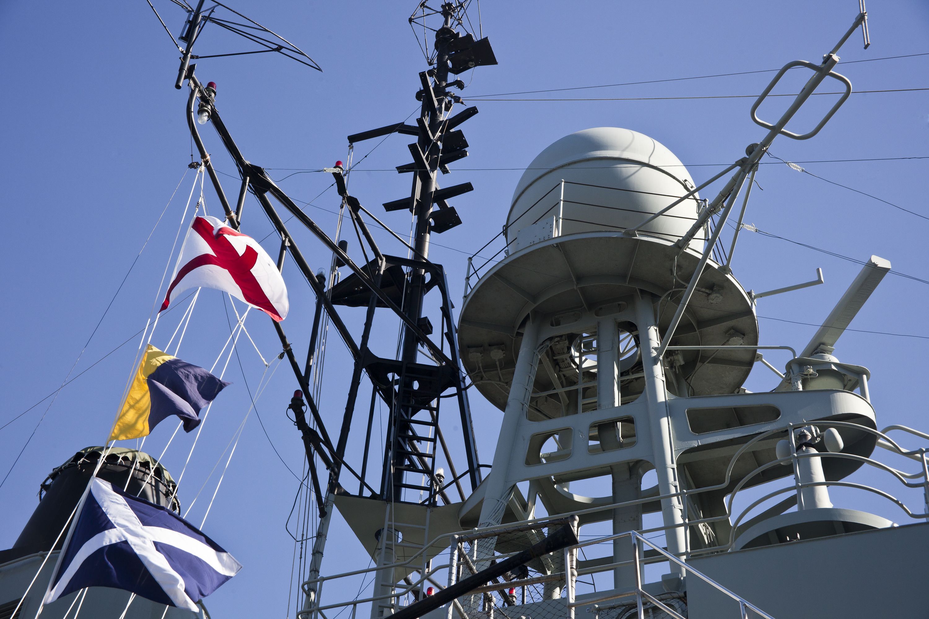 Photograph onboard a navy ship looking up at flags and radar dome.