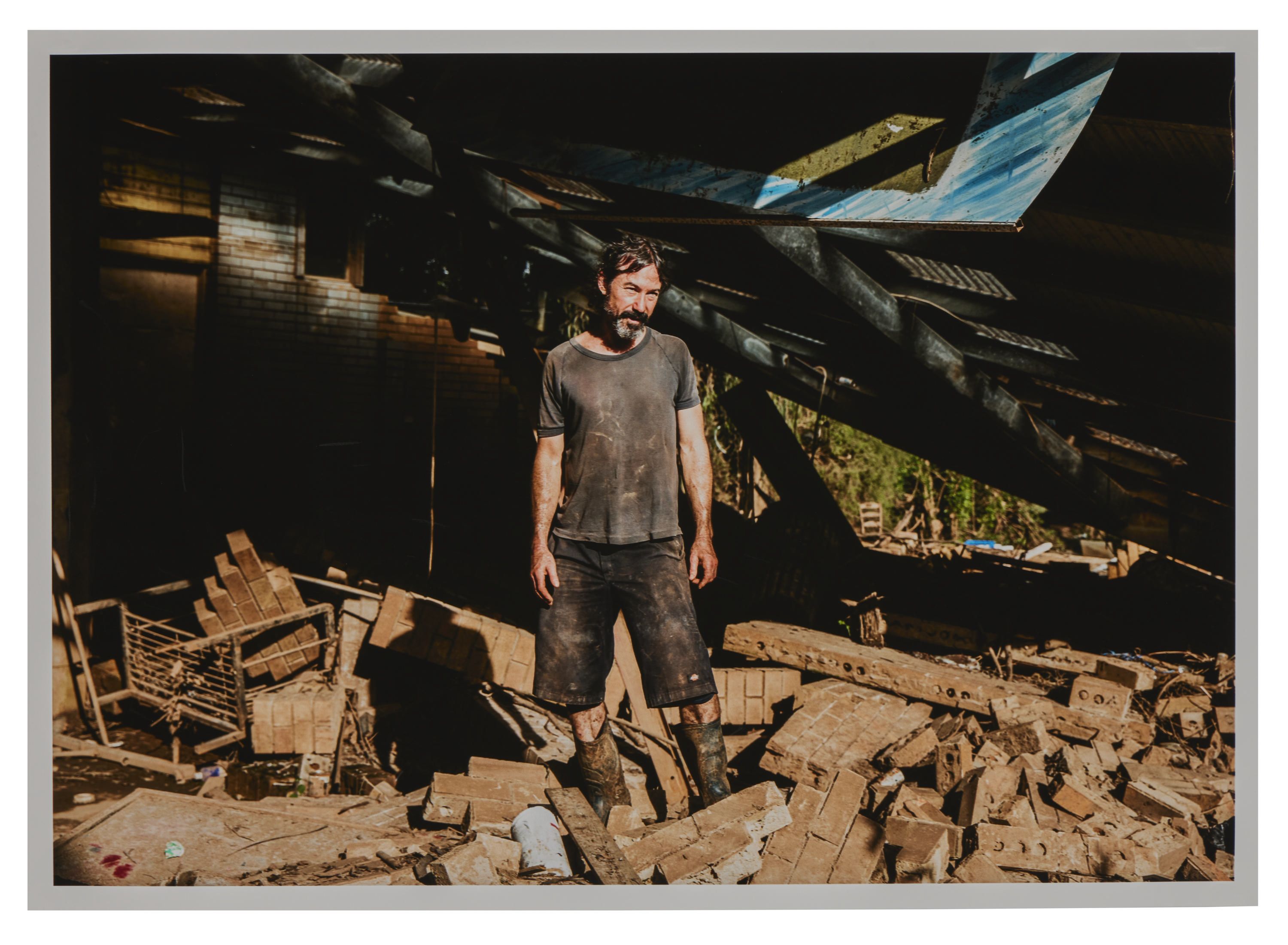 Photo of a man standing, covered in dirt and surrounded by debris. 