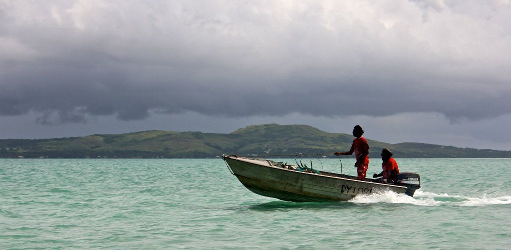 Pho taken of 2 people n a small metal boat, with an island behind them.