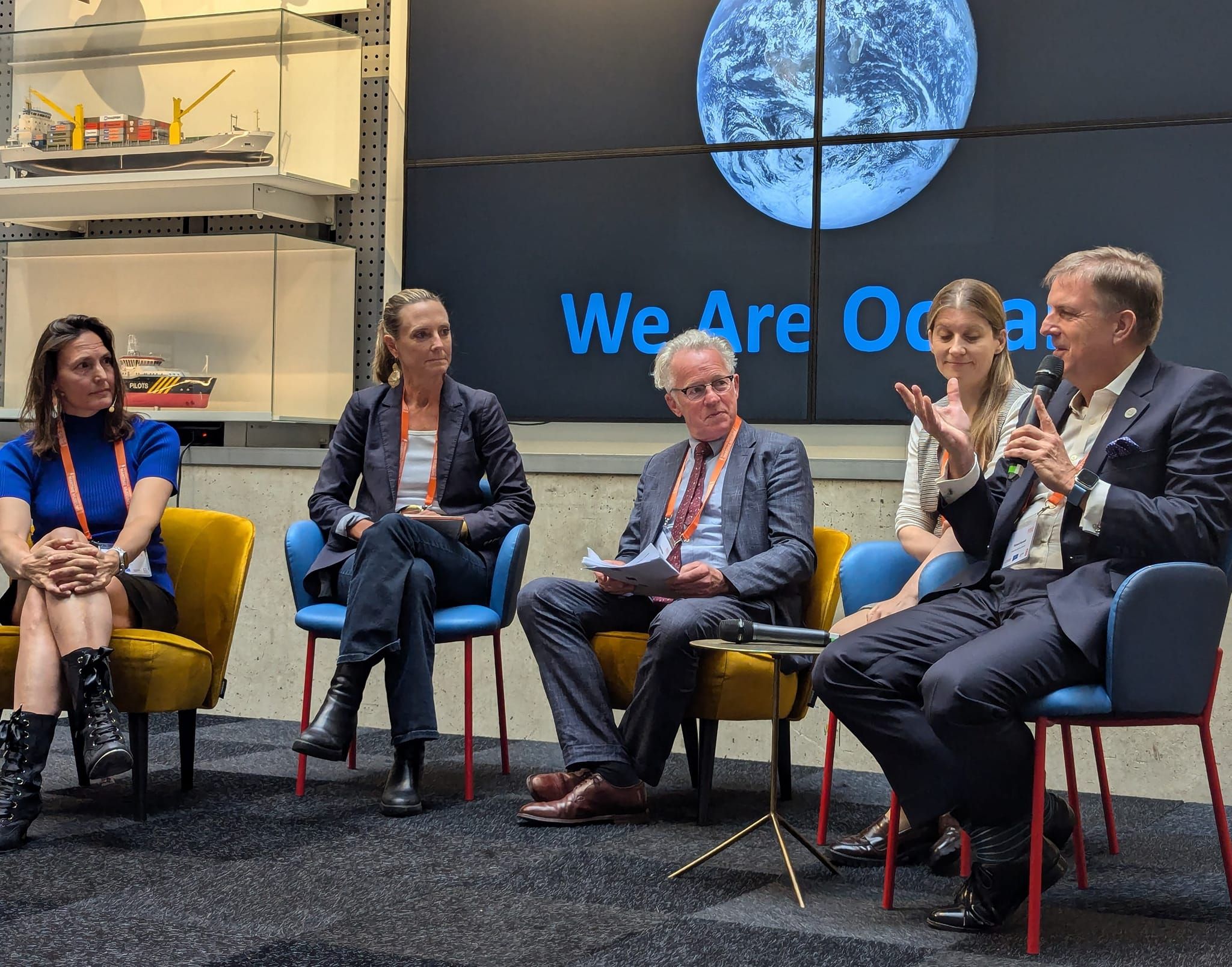 Photo of 5 people presenting while seated on a stage in a museum.