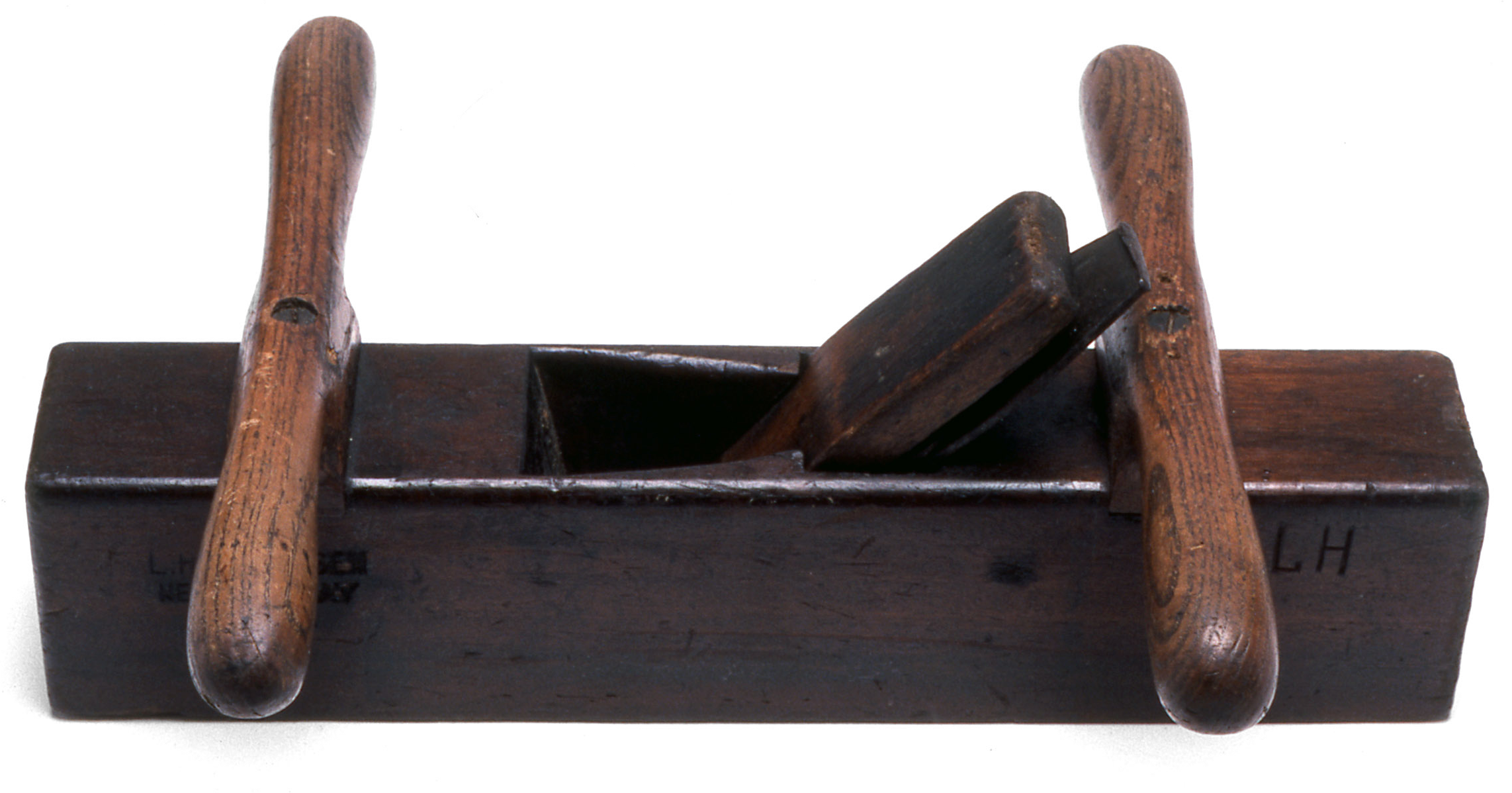 Two person plane made from hardwood with a rectangular shaped body, known as a stock, with two identical oak handles screwed across the length. An iron plane, or cutter, is situated between the two handles. The initials 'L H' are carved into the corner of one side.